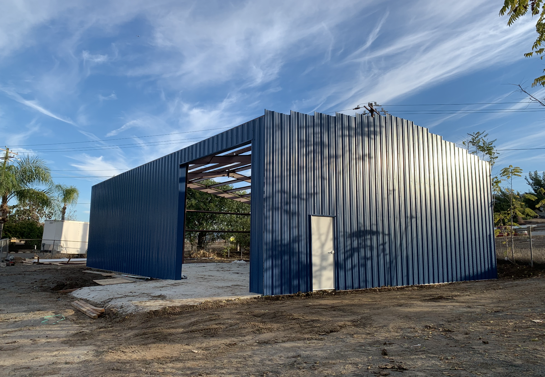 Mid construction of a metal building with build siding frames. Steel building has a large garage door towards the right side and a personal door on the corner. 