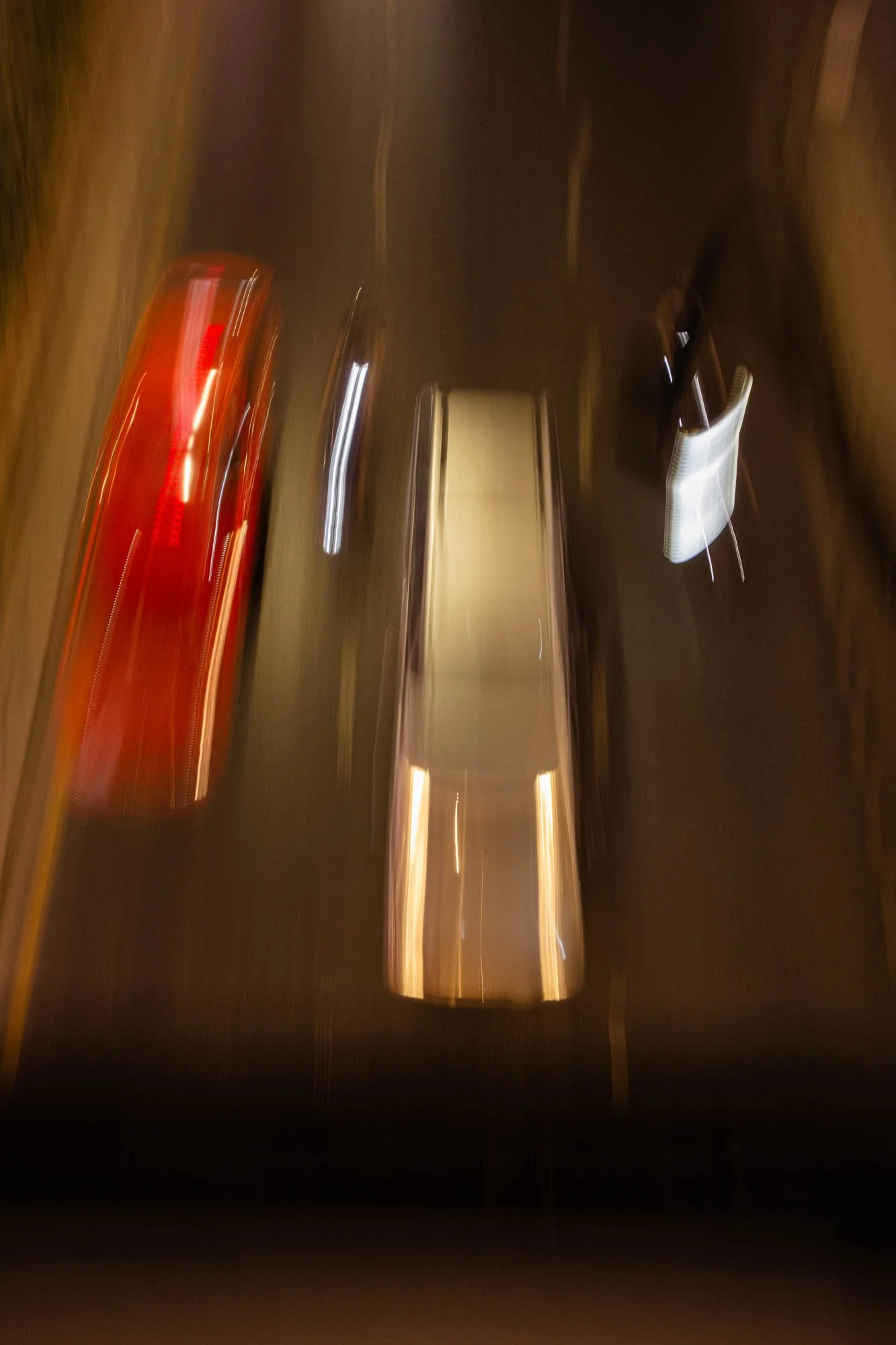 Blurred photo of three cars driving at night, viewed from above, with the middle car being silver or gray, the left car red, and the right car dark-colored.