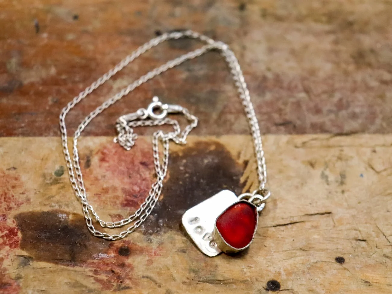A red sea glass pendant with a silver plate imprinted with the word love on a sterling silver necklace made in class