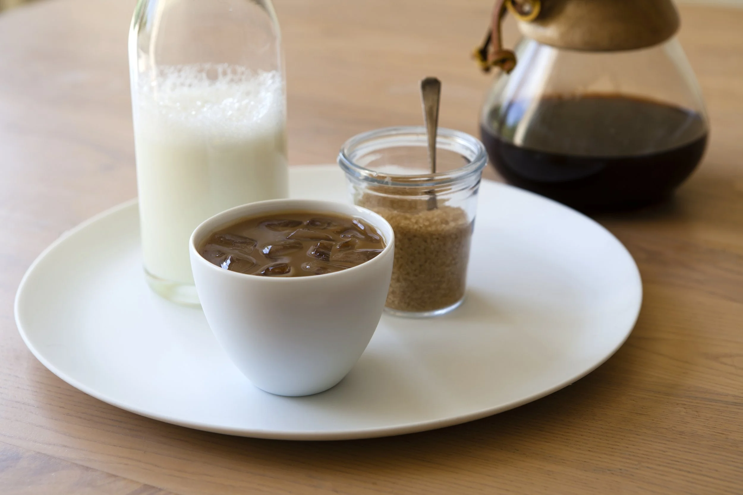 high key edit using Lightroom of freshly made iced coffee with milk and sugar all sitting on a white plate on a table.