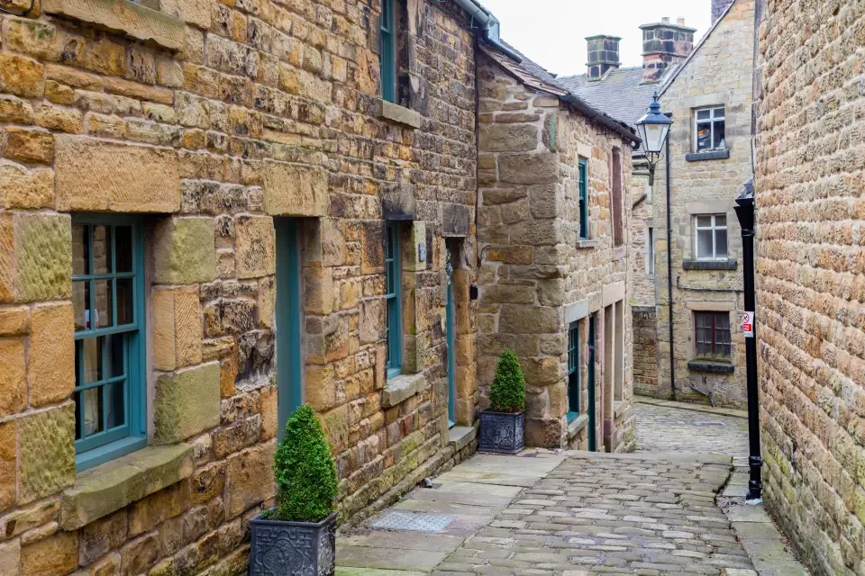 A narrow cobblestone alleyway lined with stone buildings and adorned with small potted greenery.