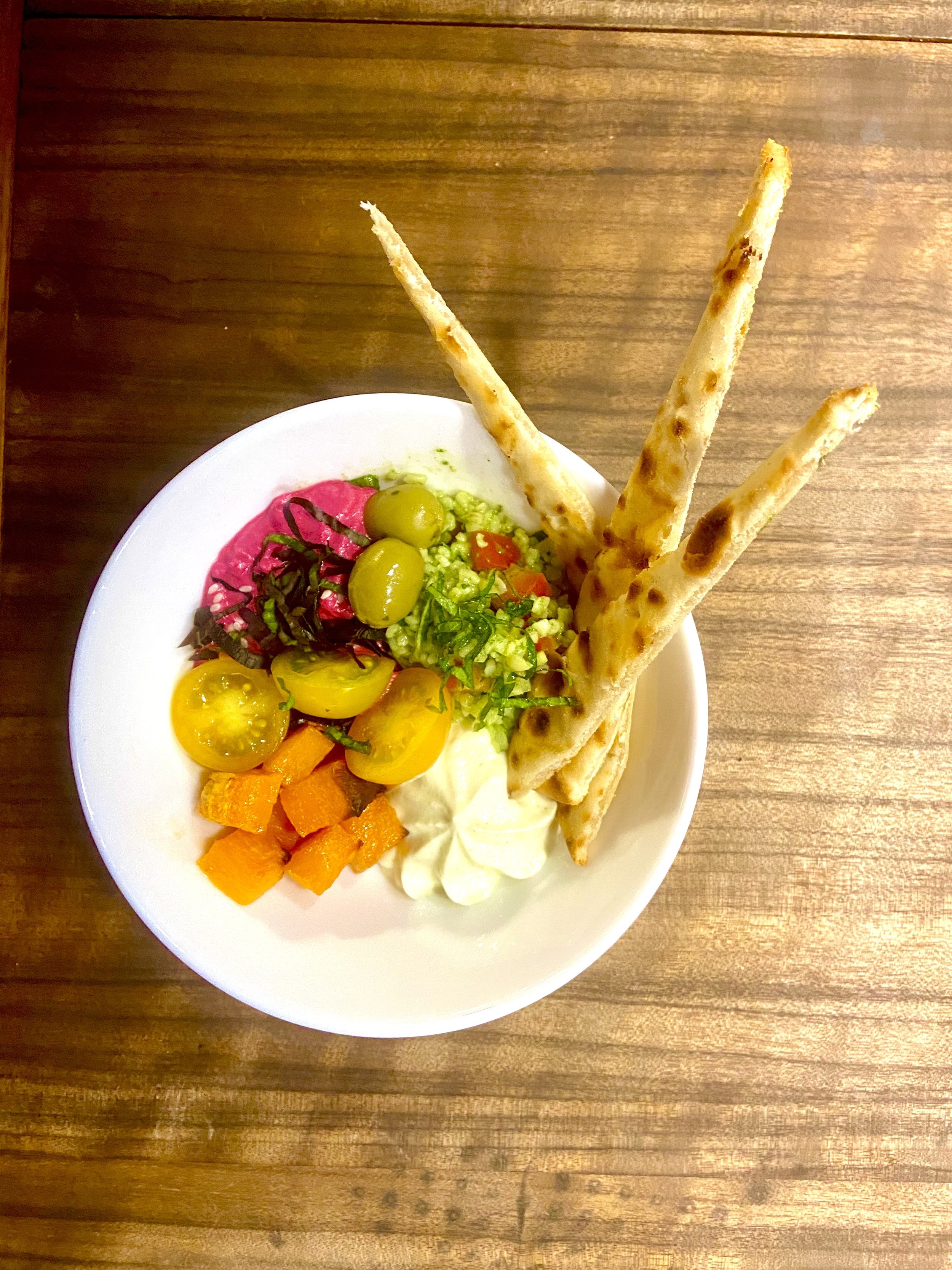 A white bowl containing salad with green and purple grapes, diced orange butternut squash, chopped green lettuce, chopped red cherry tomatoes, a dollop of creamy dressing, and three crispy breadsticks sticking out.