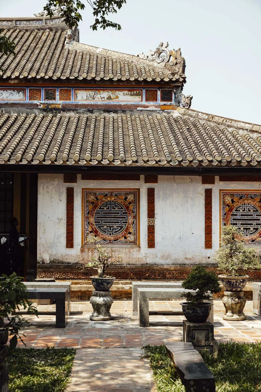 Traditional vietnamese building with tiled roof and upturned eaves, with mosaic window details and a courtyard in the foreground