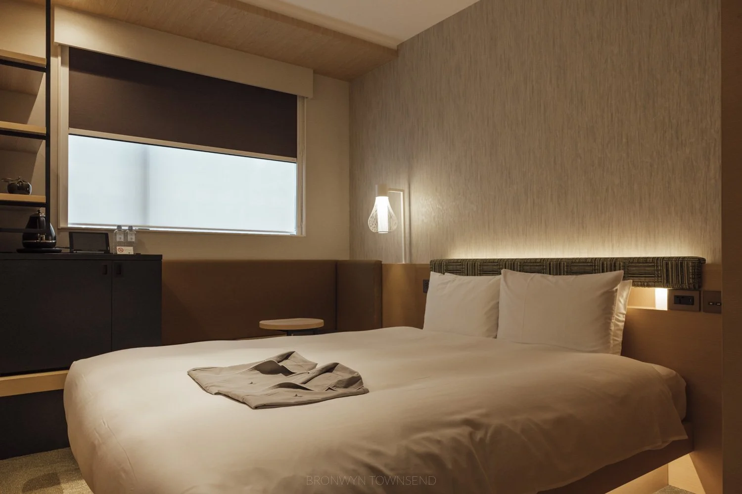 Room at Hotel 1899 Tokyo with light wood details, sand coloured wallpaper and white bedding
