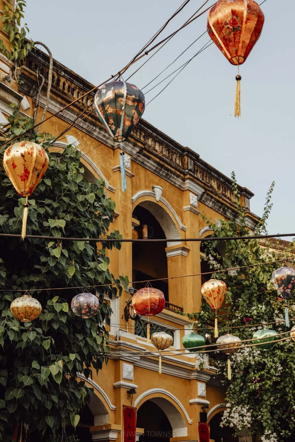 yellow arched facade with leafy vines and lanterns stung across