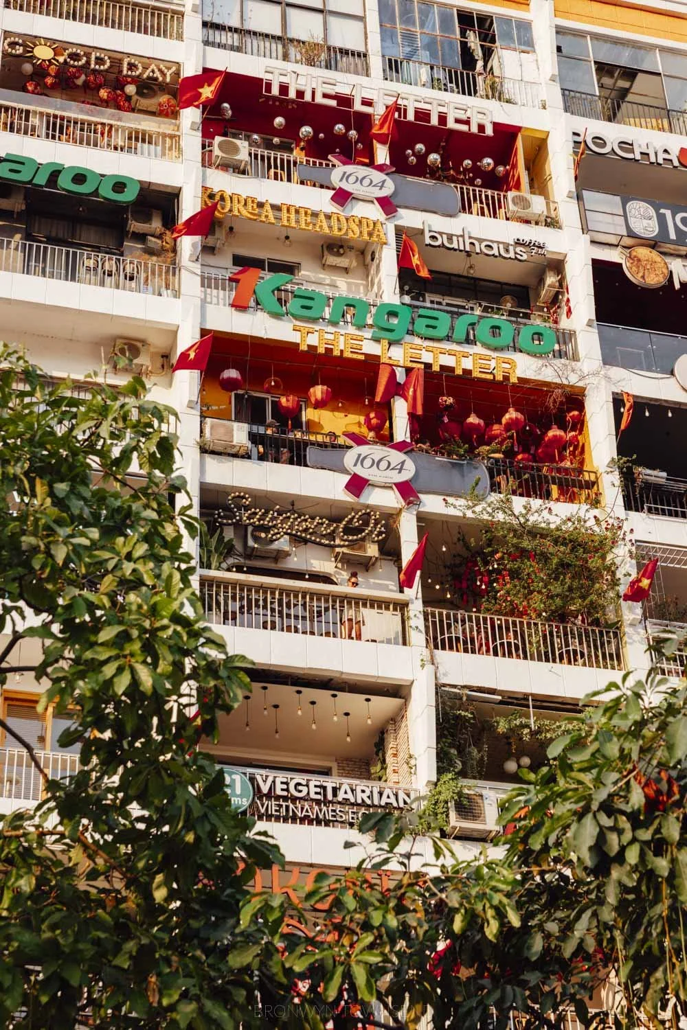 a cropped view of apartment building exterior with cafe and brand signs with trees in the front