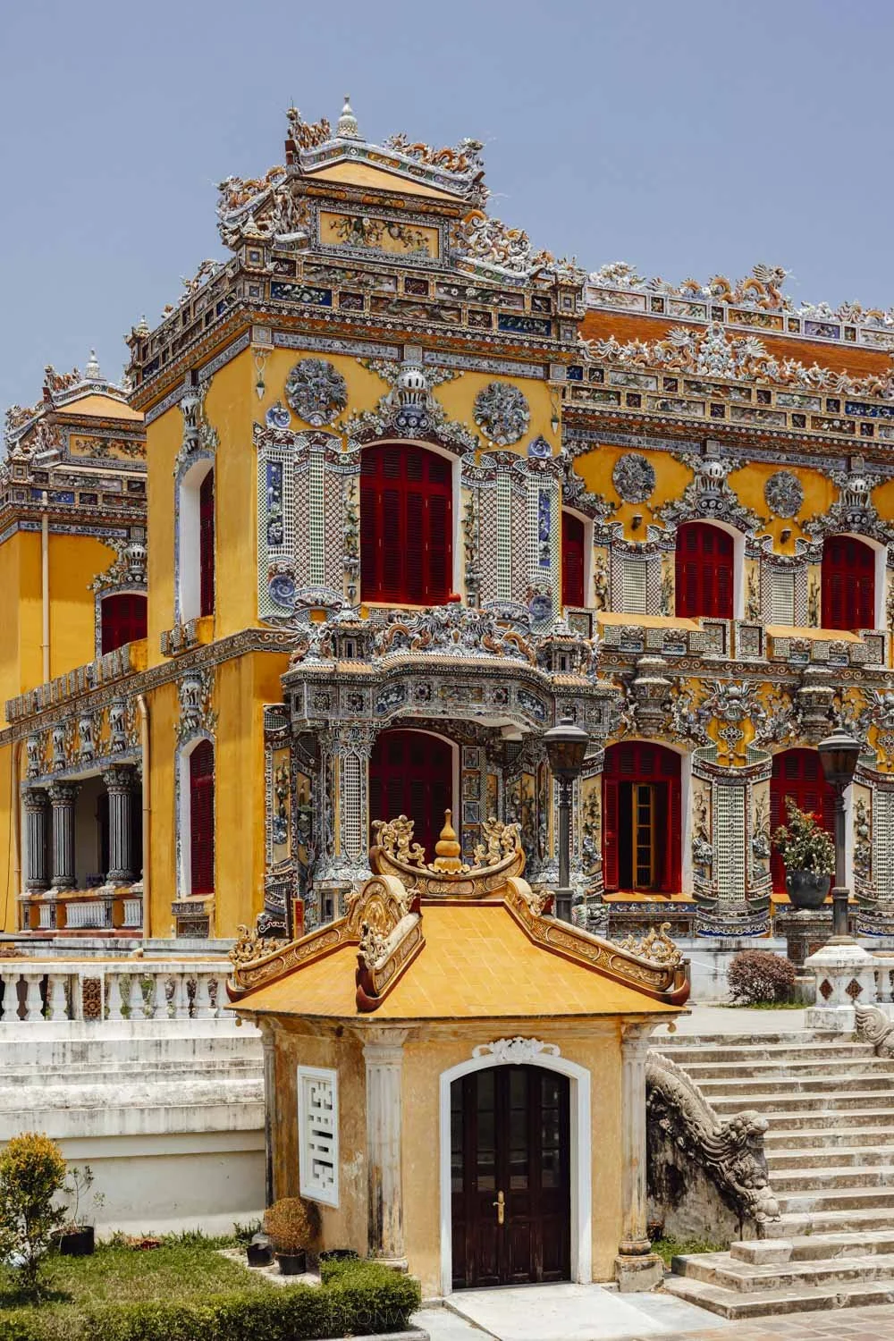 an ornately decorate yellow facade of kien trung palace at the hue citadel on a clear blue sky day