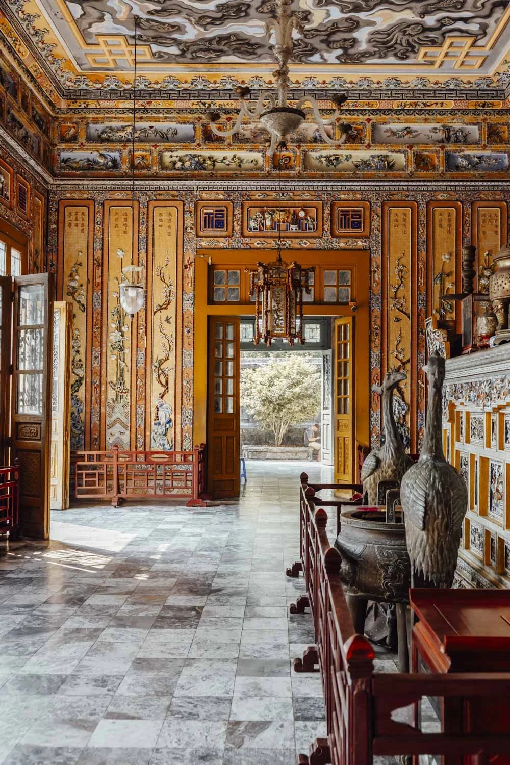 ornate blend of european and vietnamese architectural styles at the interior of khai dinh. Colourful mosaic details, large windows and doors, and a simple chandelier fill the room.