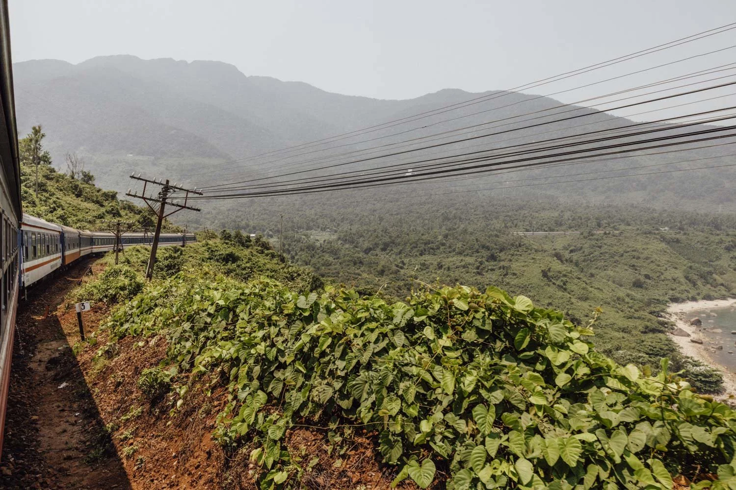 view from the window on the train on the hai van pass, with green mountainside and the train angling to the right around a bend