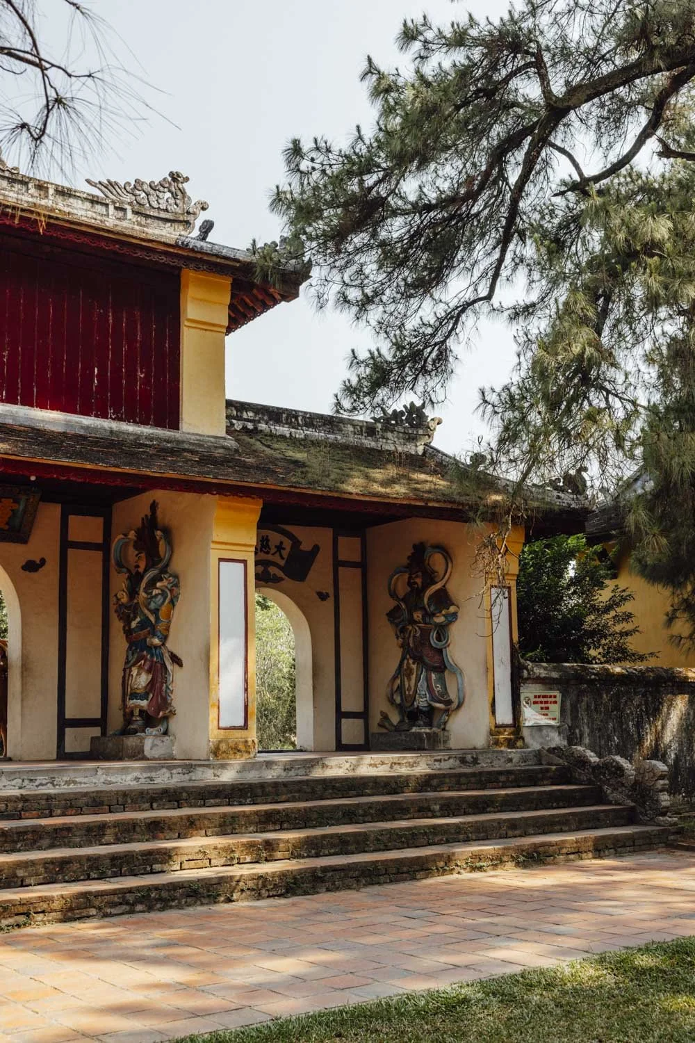 Yellow temple gate with the buddhist gods and pines at Thien Mu Pagoda, Hue