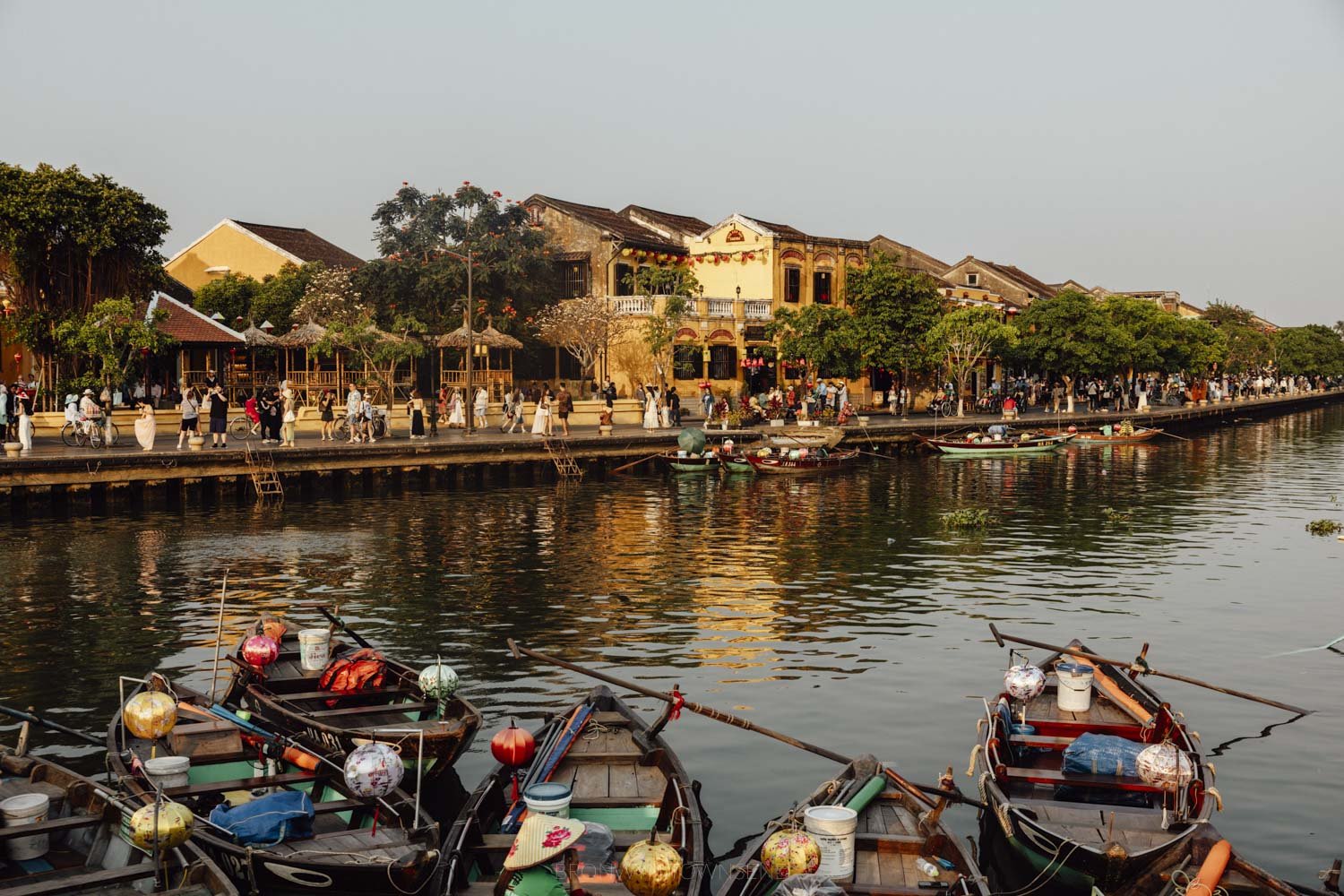 View of Hoi An Old Town riverfront with yellow buildings and palm trees