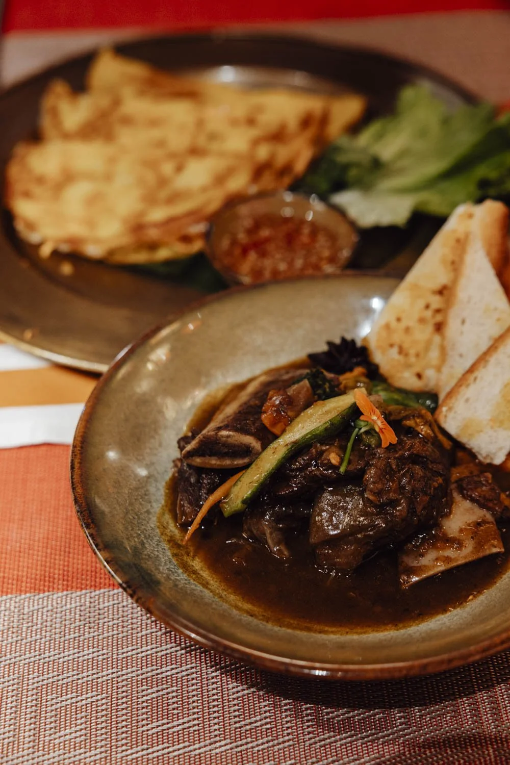 A bowl with slow cooked beef in the foreground and crispy vietnamese pancakes out of focus in the background