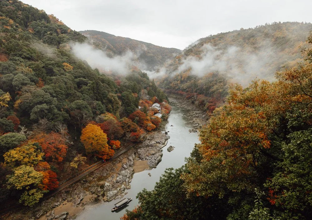 hills of arashiyama with hozugawa river running through the middle, autumn foliage on the hillsides, and low clouds in the valley.