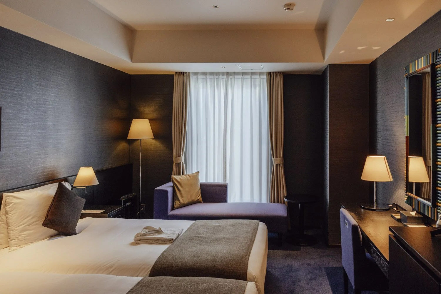 Room at the gate hotel by hulic in Asakusa Tokyo with dark grey wall paper, white bedding, and lit lamps