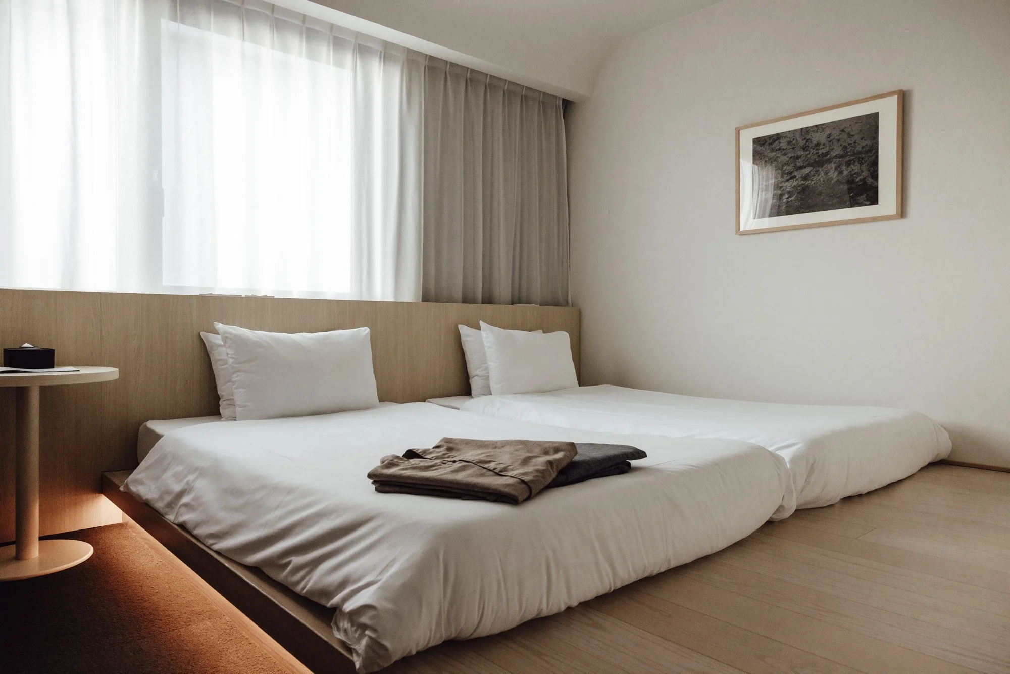 Japanese style room with minimalistic design, sheet curtains, and beds on a raised wooden tier at SOKI Kanazawa Hotel.