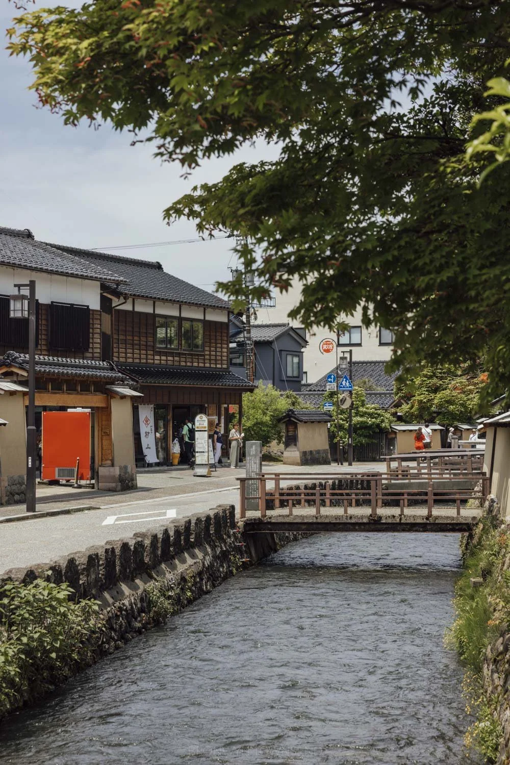 The canal and streets of Nagamachi samurai district with leafy green maple trees in the foreground.