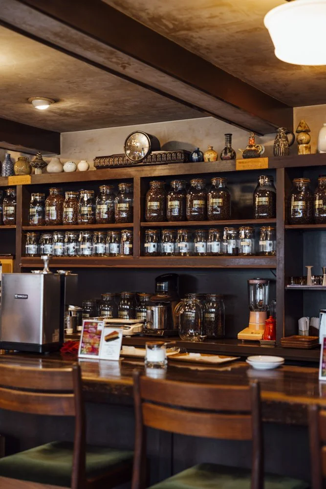 Dark wooden cafe interior with glass jars filled with coffee beans on the shelves and green velvet stools at the bar