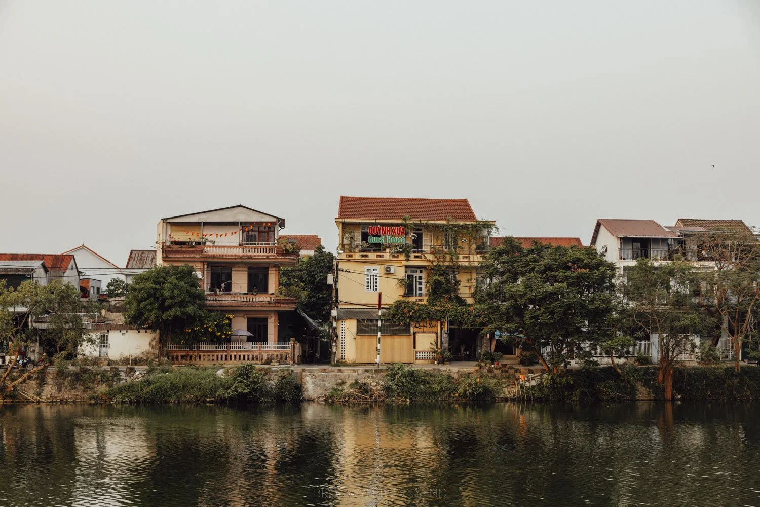 Buildings in shades of pink and yellow along the perfume river, with the river and trees in the foreground