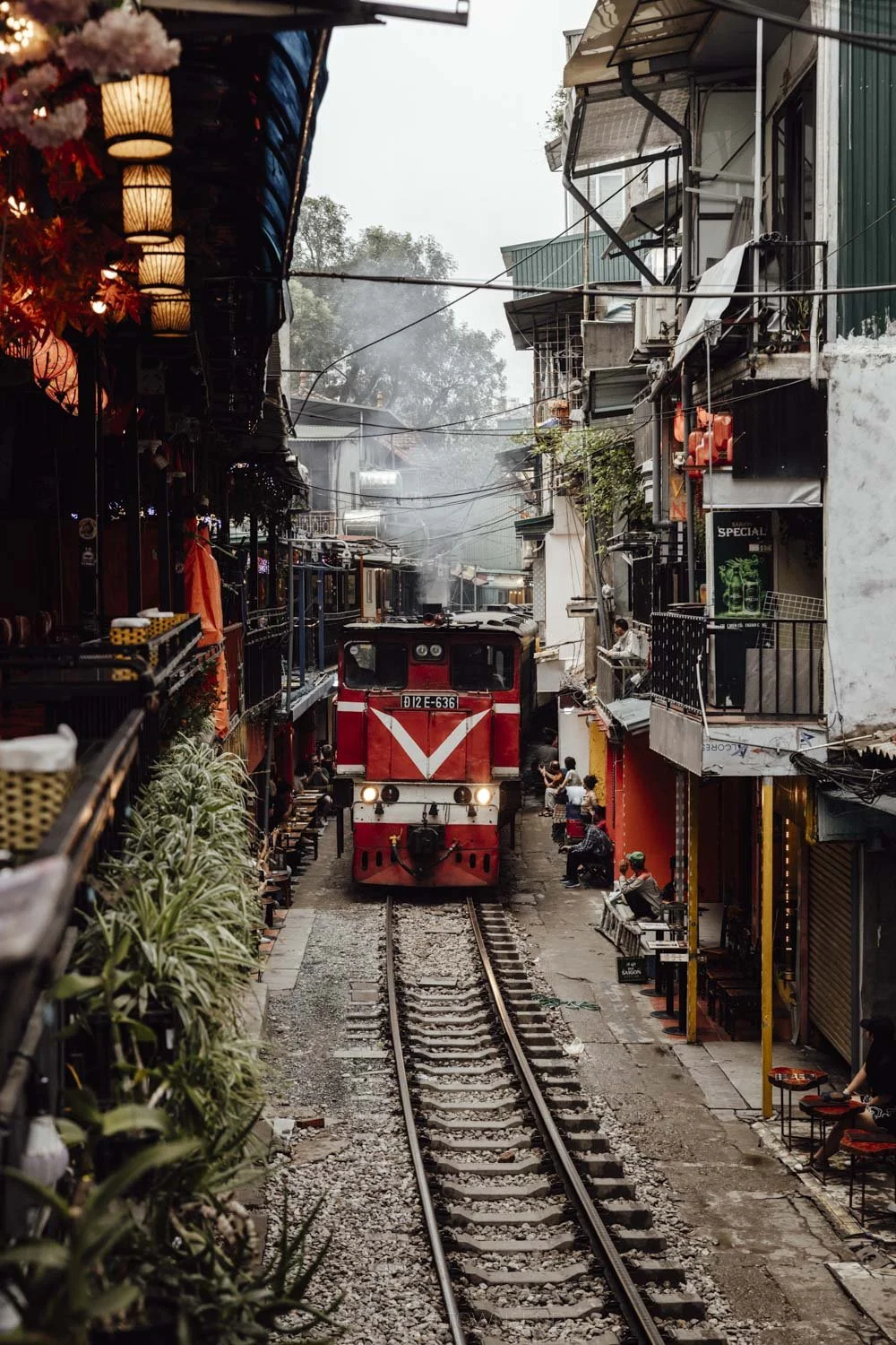 old red steam train coming along train street hanoi between narrow buildings