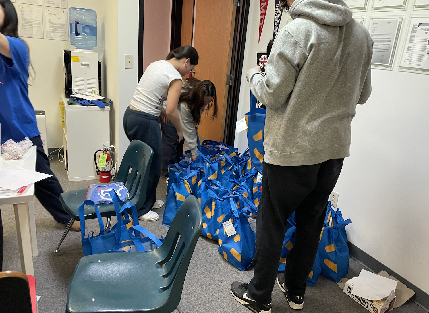 People organizing blue gift bags with orange accents in a room, possibly for an event or charity.