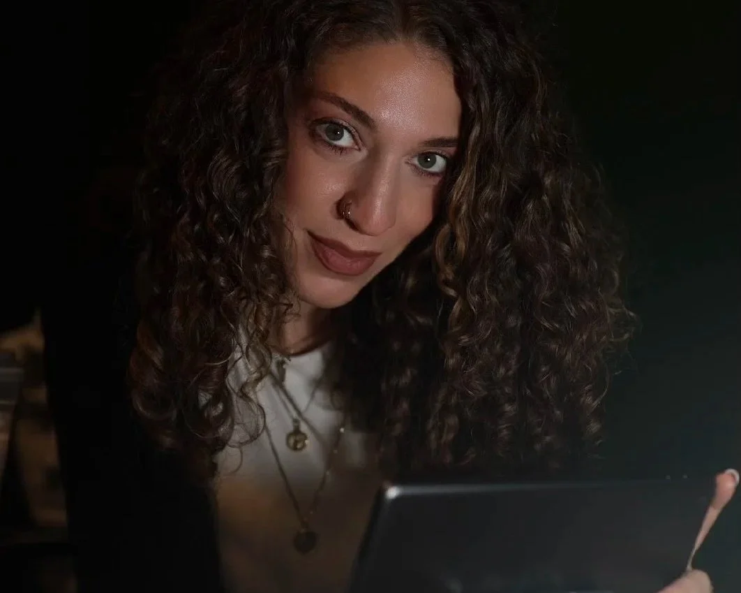 Young woman with curly hair and blue eyes looking at a tablet in a dark room.