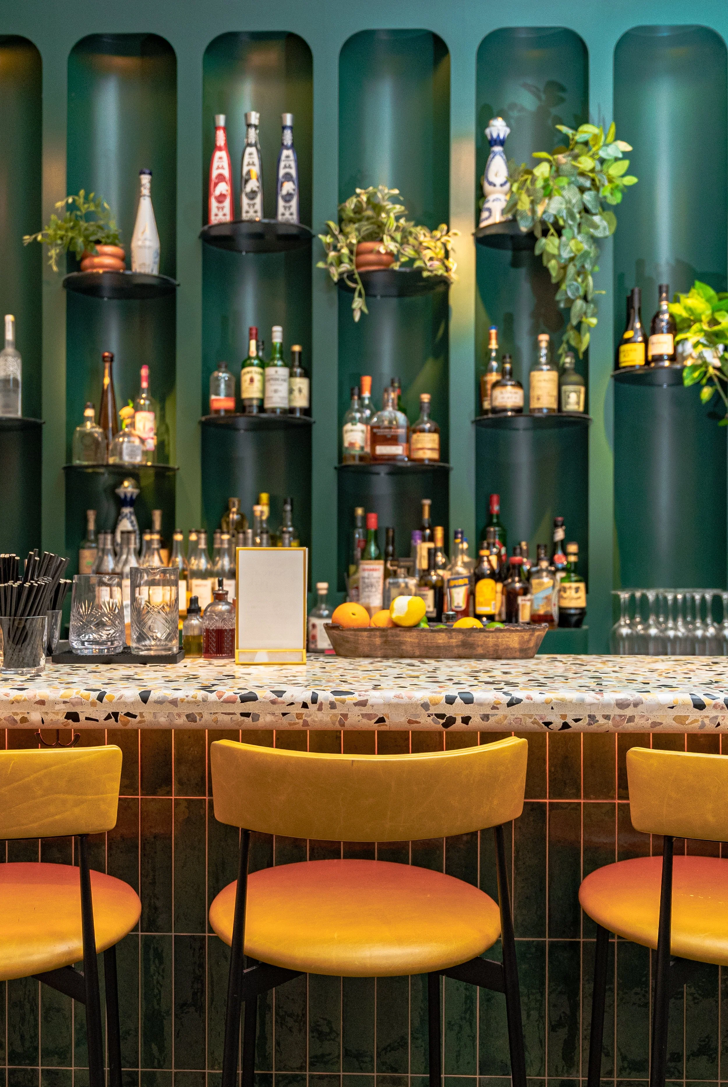Deep emerald bamboo design bar back with bright yellow bar chairs. Eclectic bar.