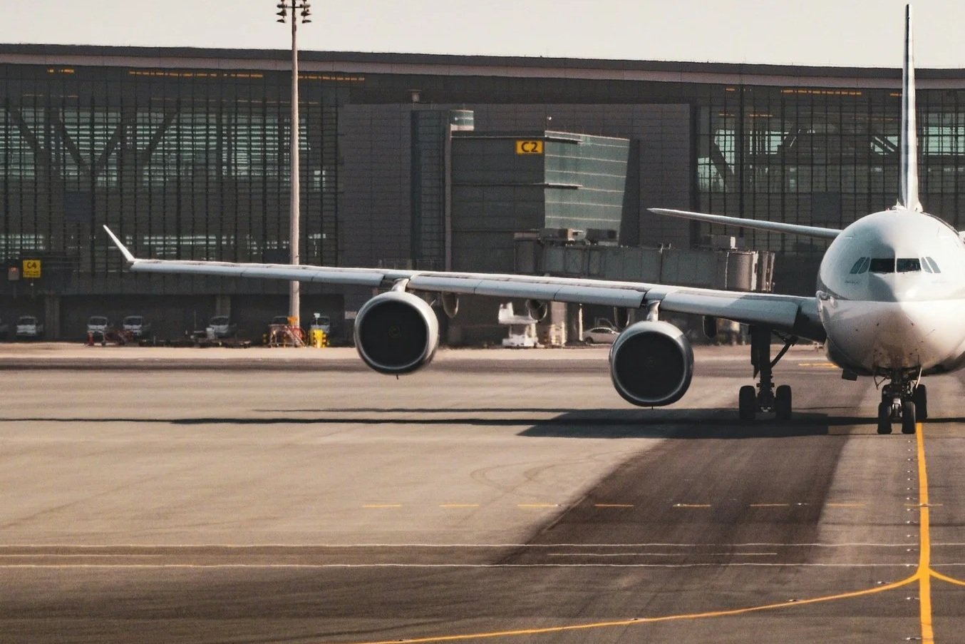 An airplane taxiing on the runway at an airport, with a modern terminal building in the background.