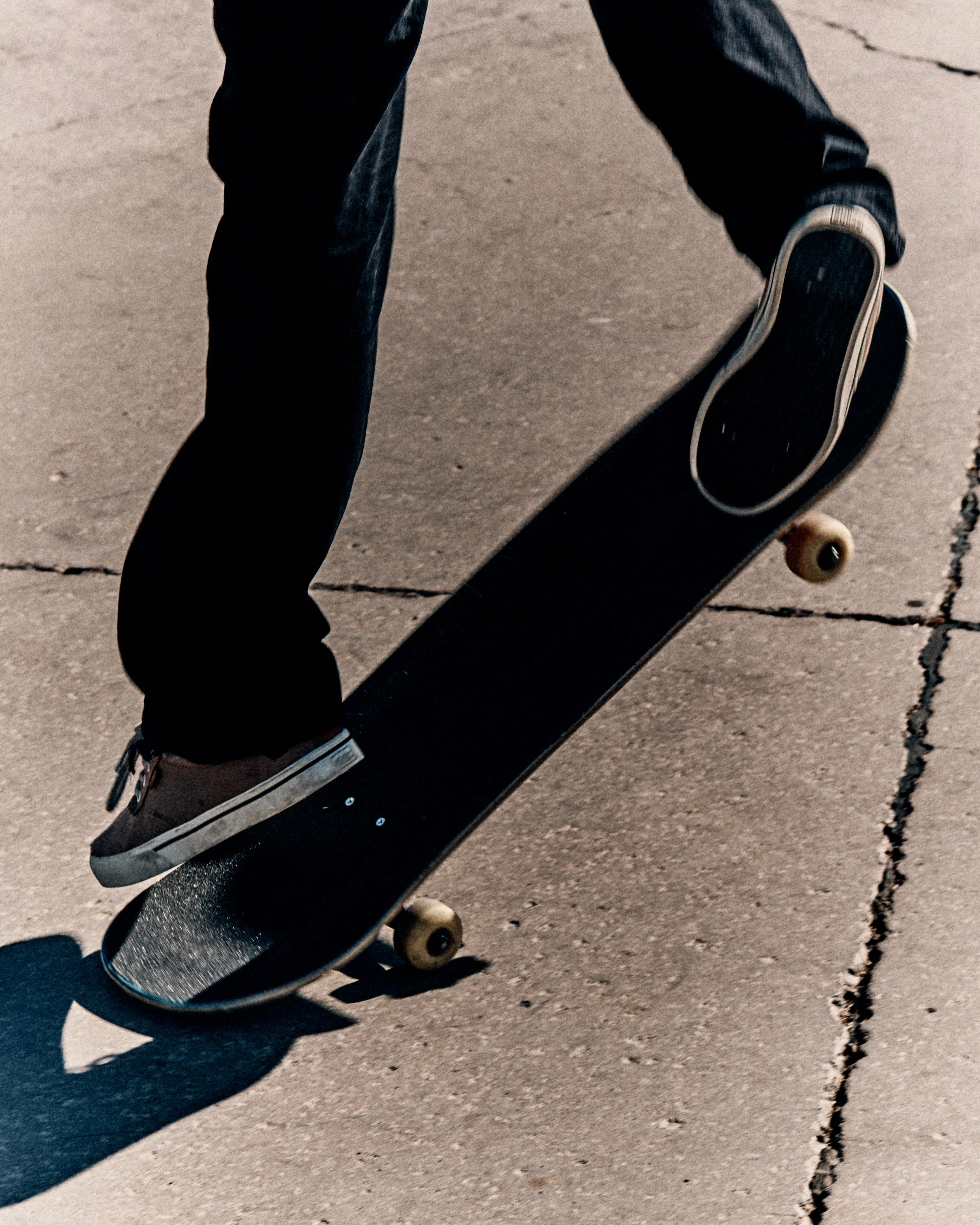 Close-up of a skateboarder performing a trick on a concrete sidewalk, wearing black pants and gray shoes.