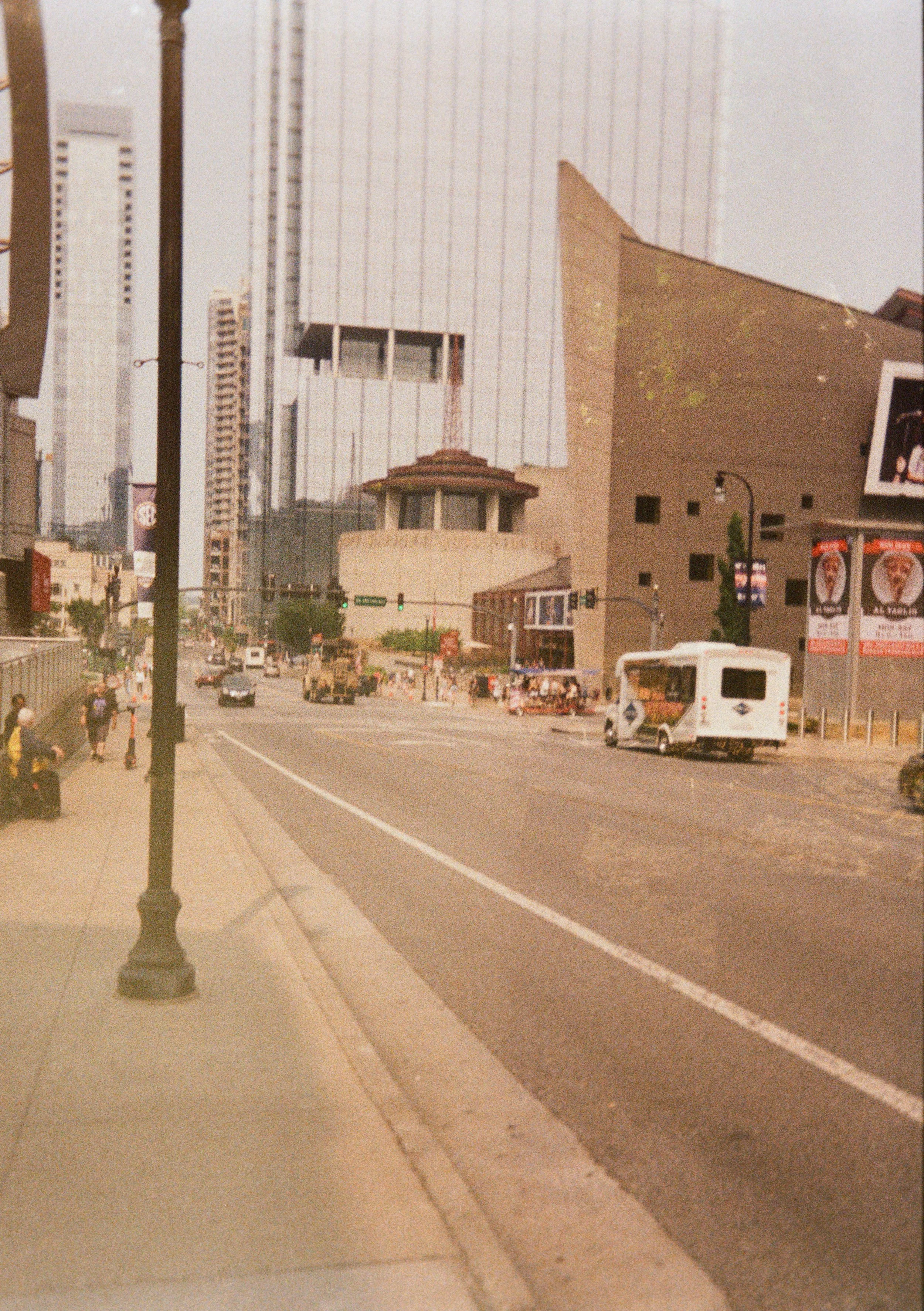 Urban city street scene with tall buildings, cars, and a food truck on the right side of the street.