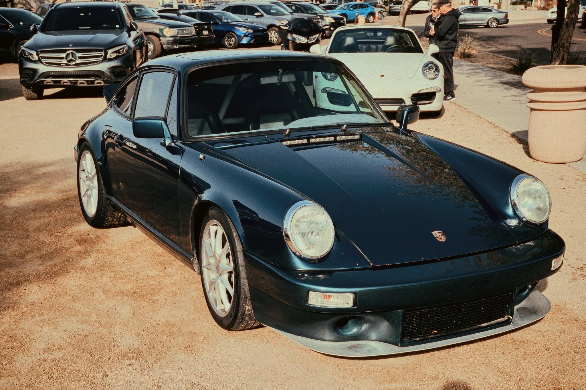 Black classic Porsche sports car parked outdoors with other cars and people in the background.
