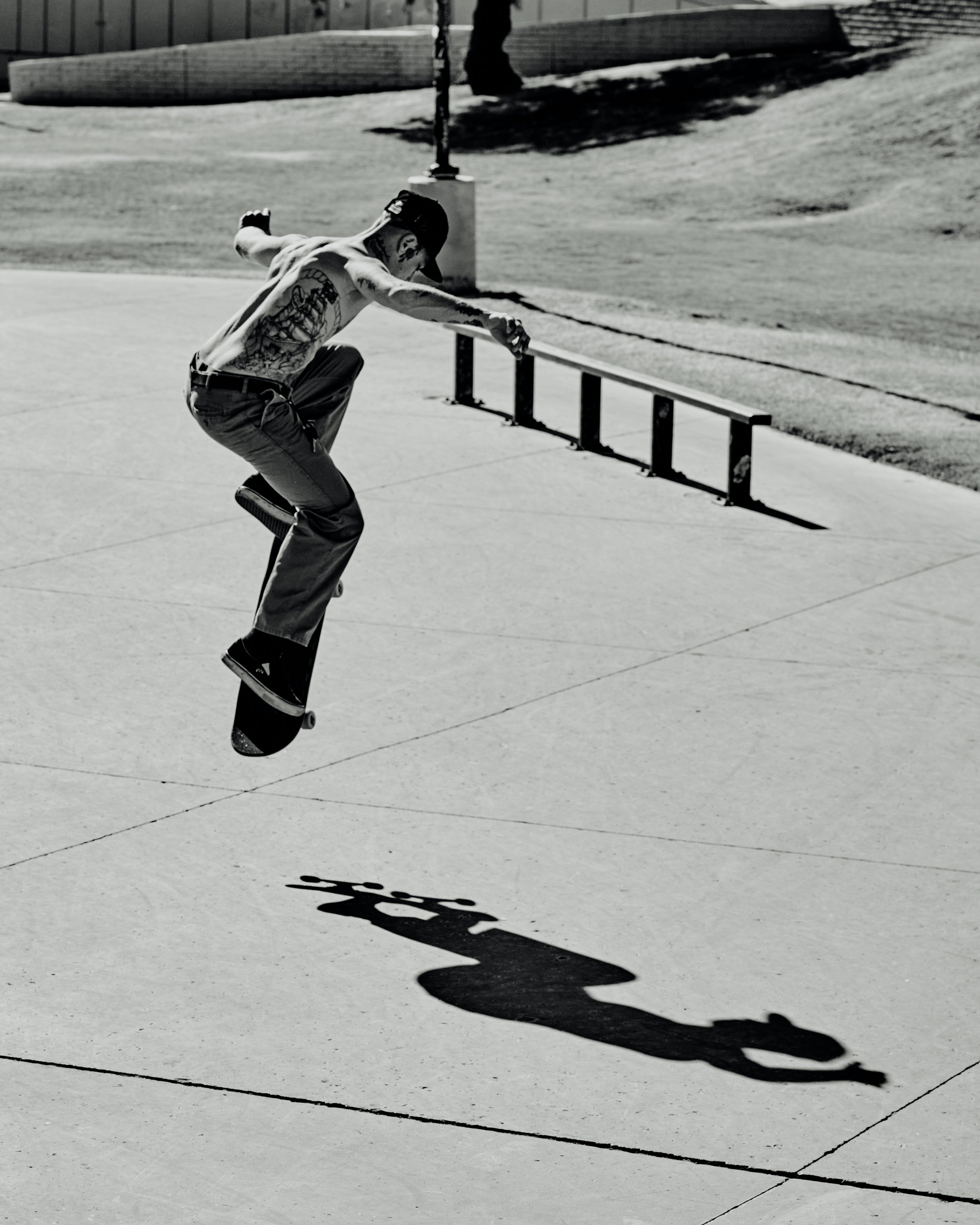Skateboarder in mid-air performing a trick at a skate park, with emphasis on his shadow cast on the ground.