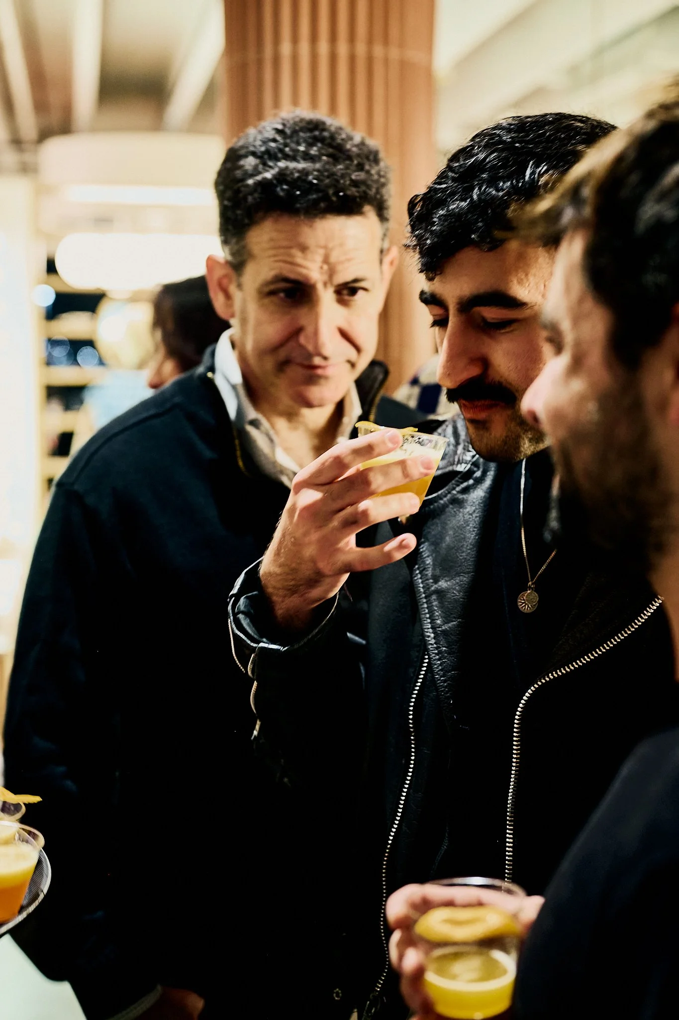 Three men at a social gathering, holding drinks and engaging in conversation.