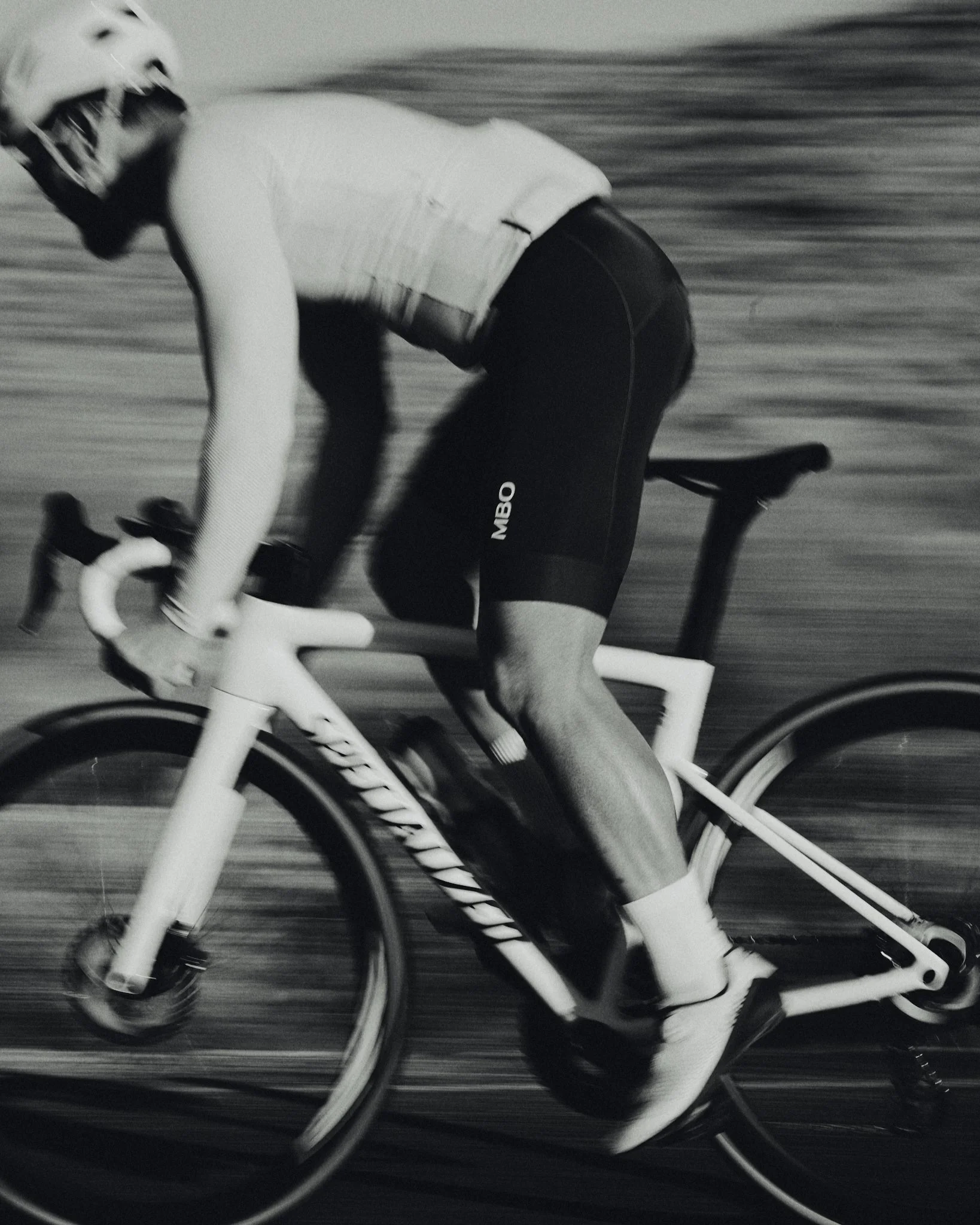 A cyclist wearing a helmet and athletic gear riding a bike at high speed outdoors, with motion blur indicating fast movement.
