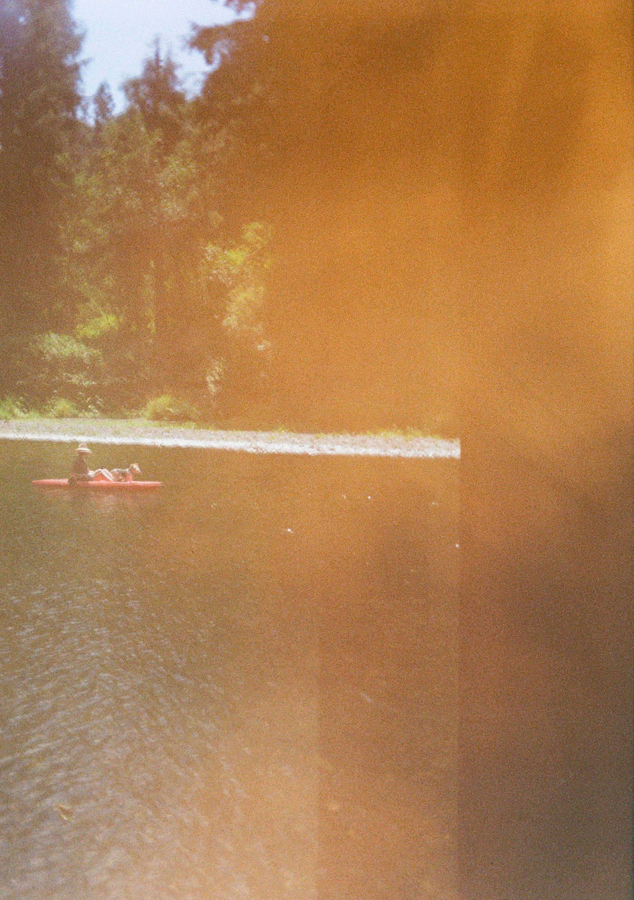 Person in a life jacket kayaking on a river with trees in the background.