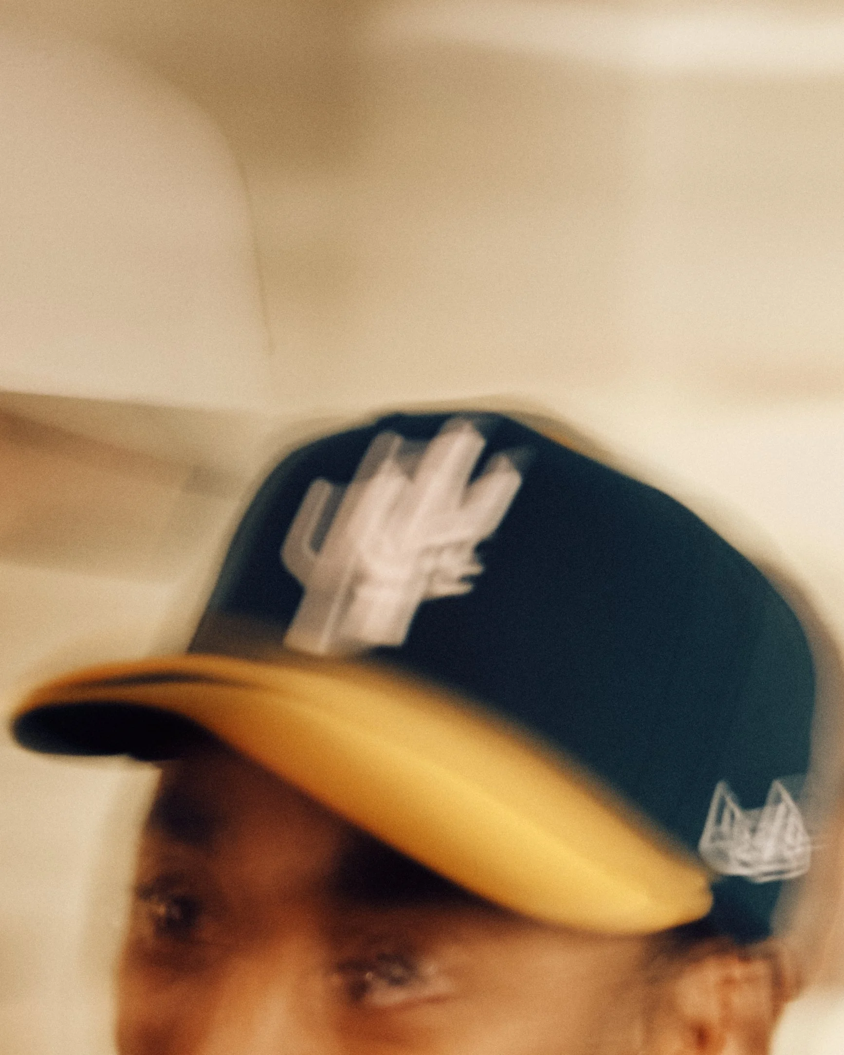 Close-up of a person's head wearing a green and yellow baseball cap, with their face partially visible.