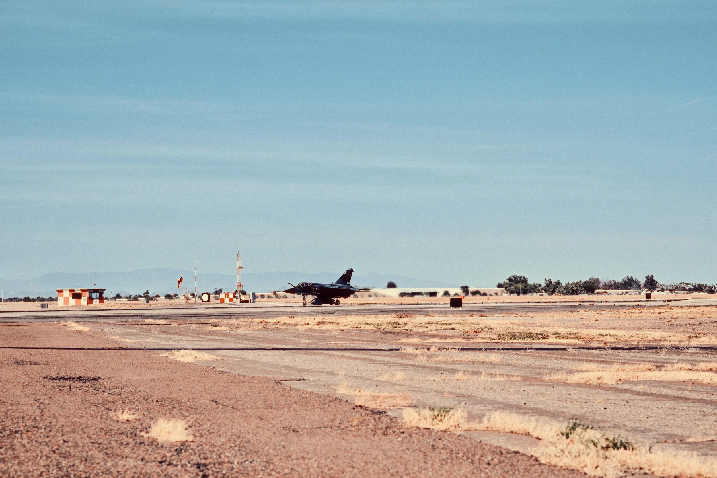 Fighter jet speeding along desert runway with clouds in the sky.