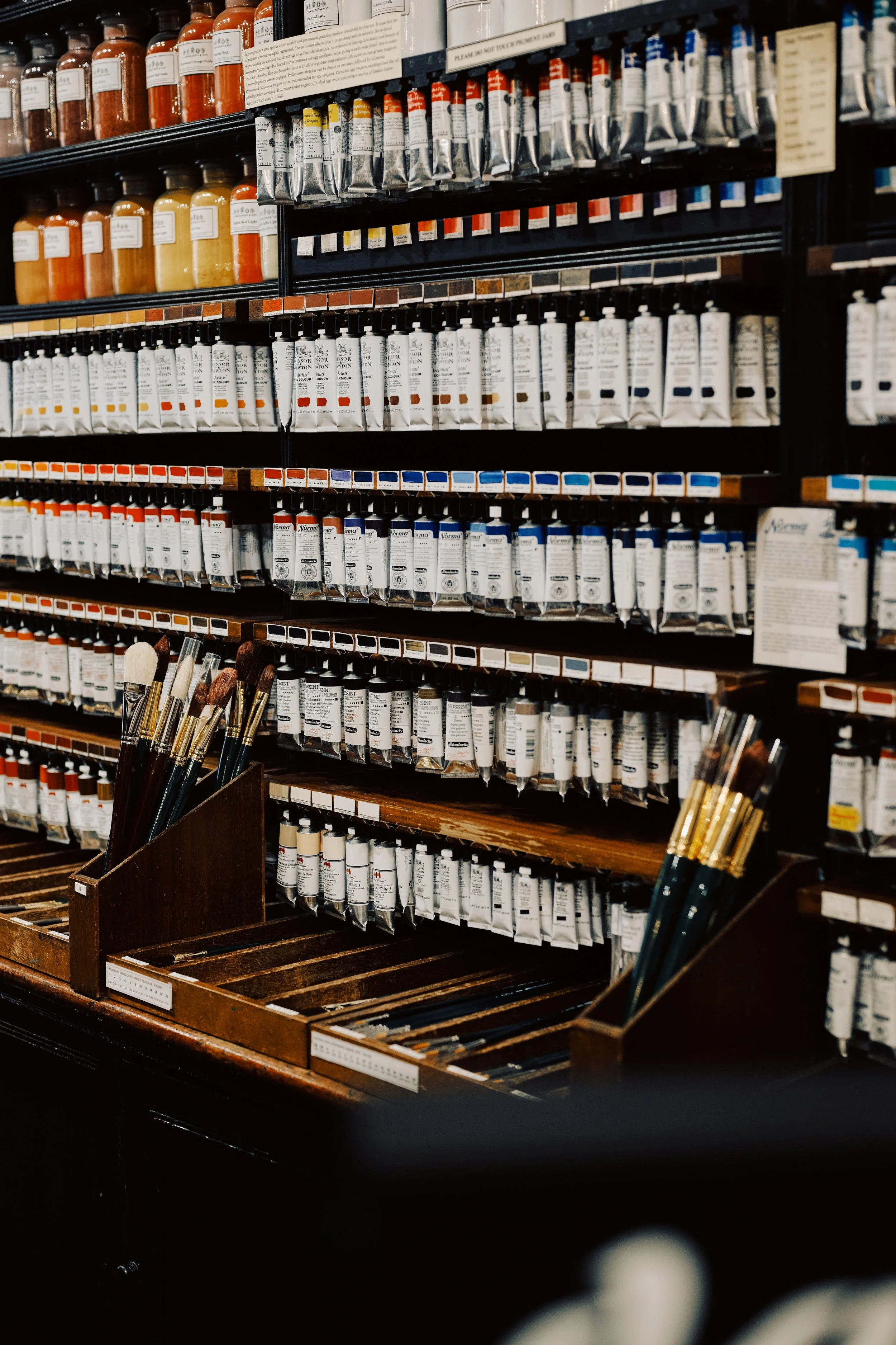 Art supplies display with tubes of oil or acrylic paint and paintbrushes in a store.