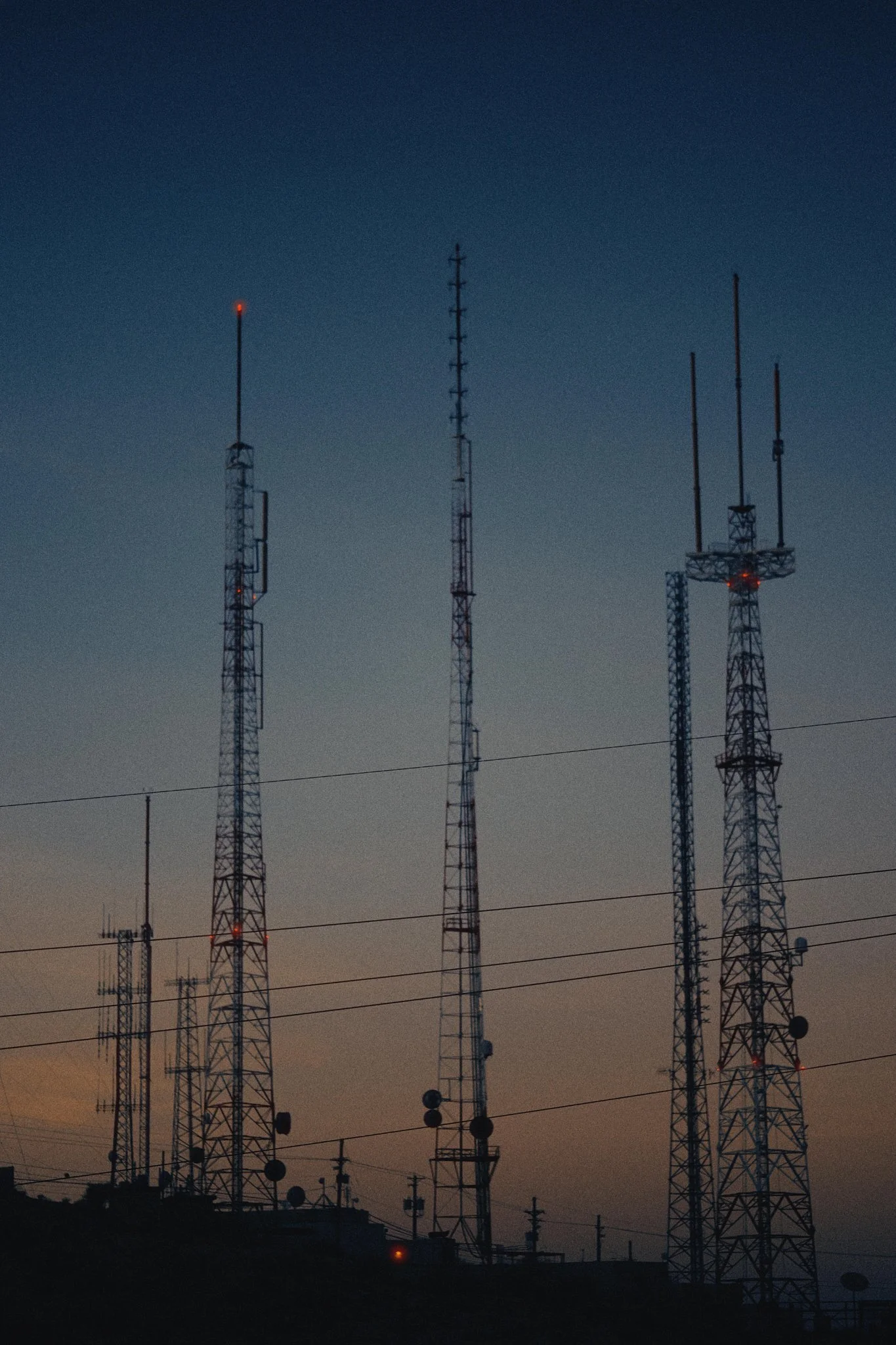 Silhouettes of multiple communication towers against a twilight sky.
