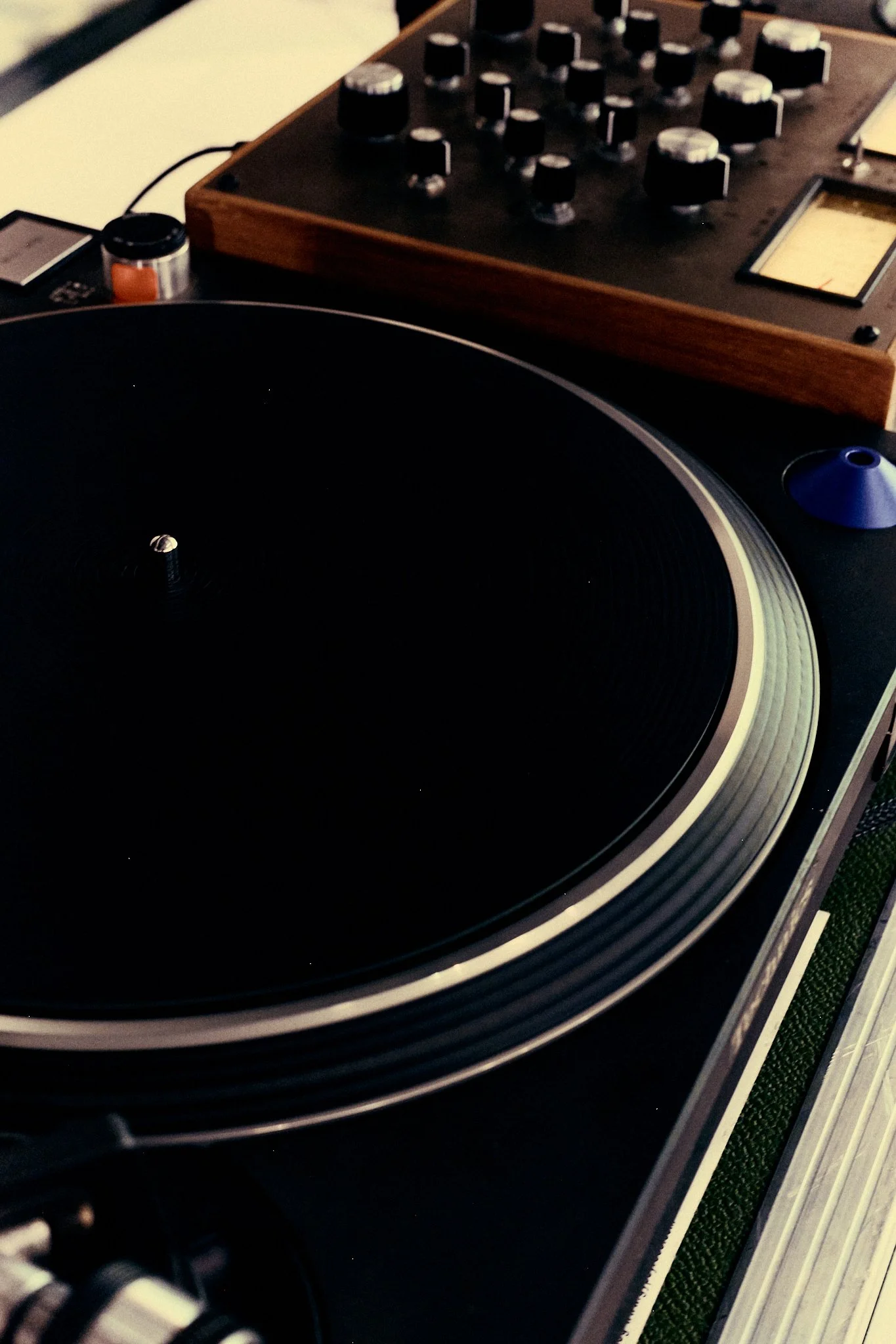 Close-up of a black vinyl turntable with a wooden DJ mixer in the background.