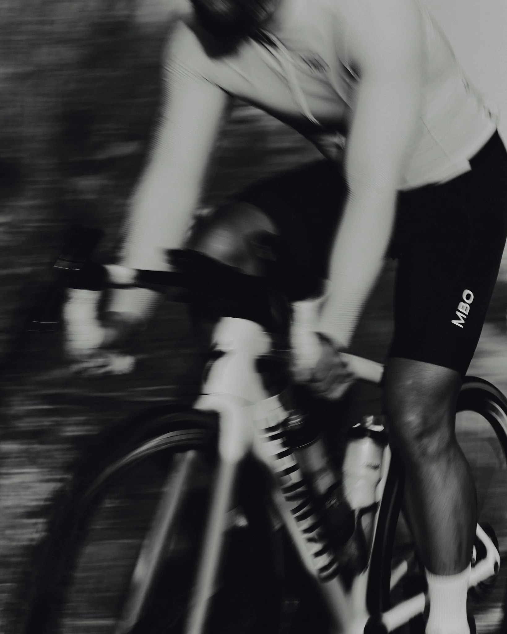 A person riding a bicycle, wearing a jersey with the letters MBO, with motion blur.