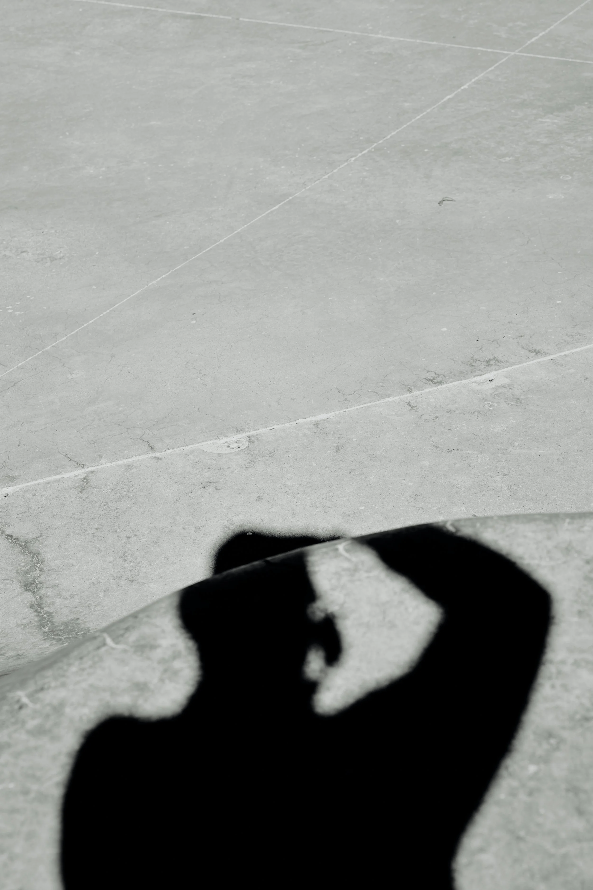 Shadows of a person on a concrete surface, with one hand making a gesture resembling an 'OK' sign.