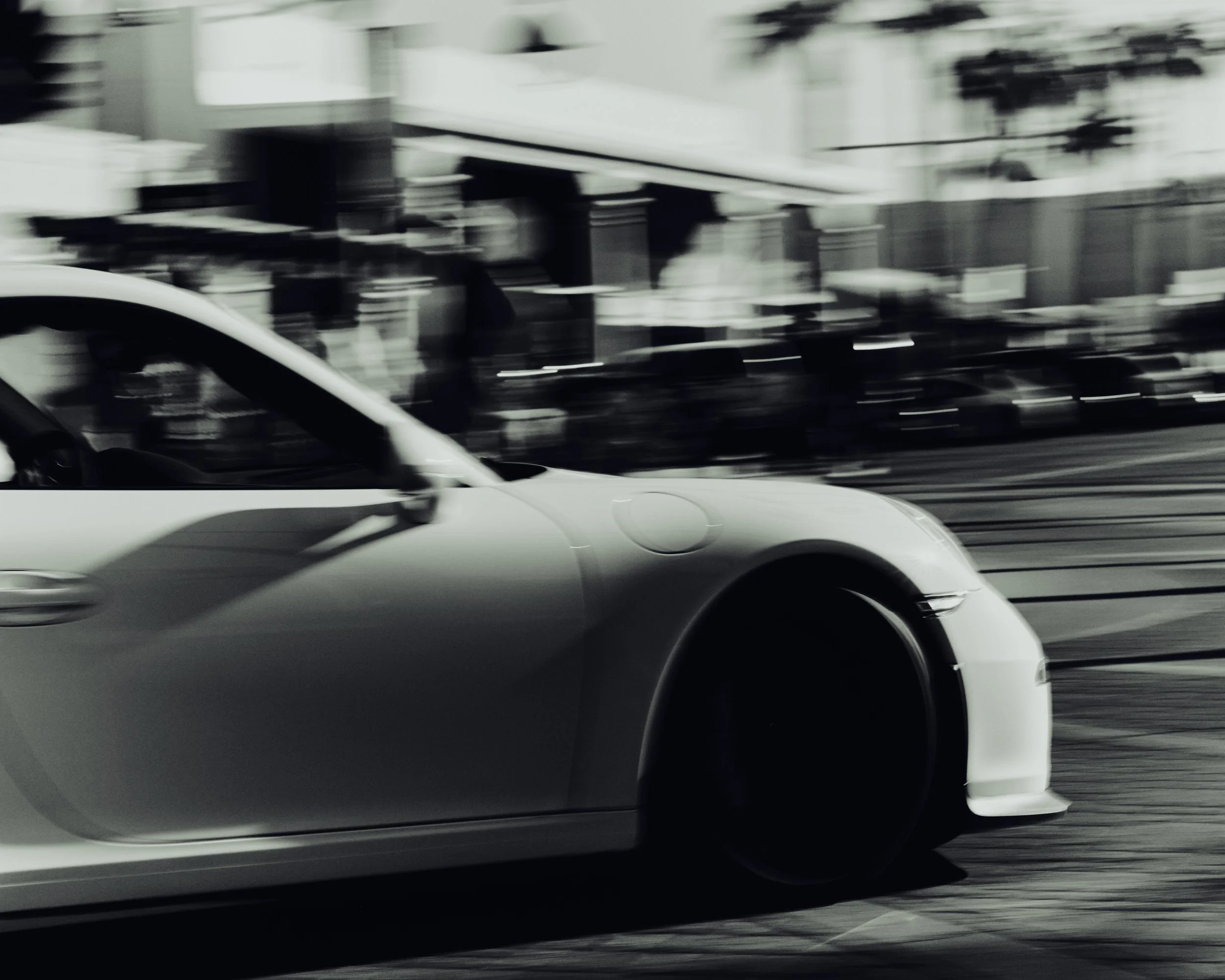 A white sports car driving quickly on a city street, captured in motion blur.