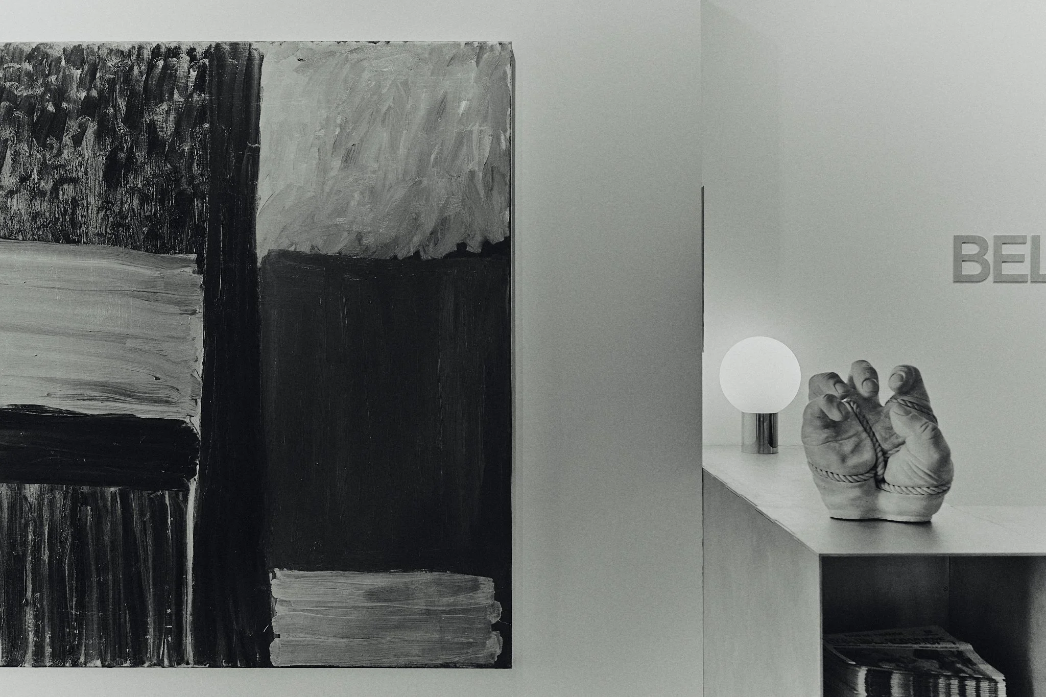 Black and white abstract painting on a wall next to a modern side table with a table lamp and a ceramic sculpture of boxing gloves.