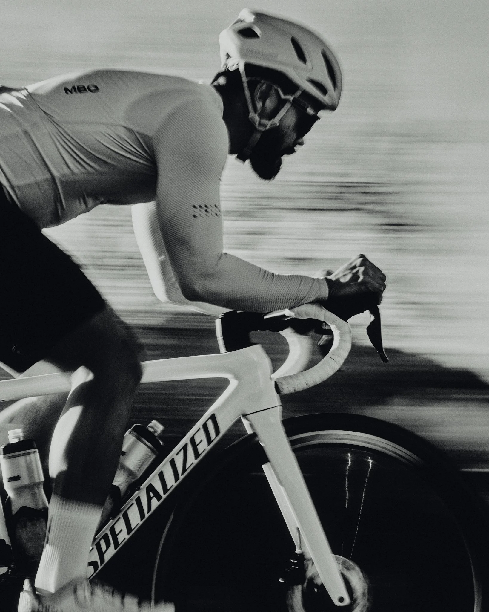 A male cyclist wearing a helmet and cycling apparel riding a Specialized road bike at high speed.