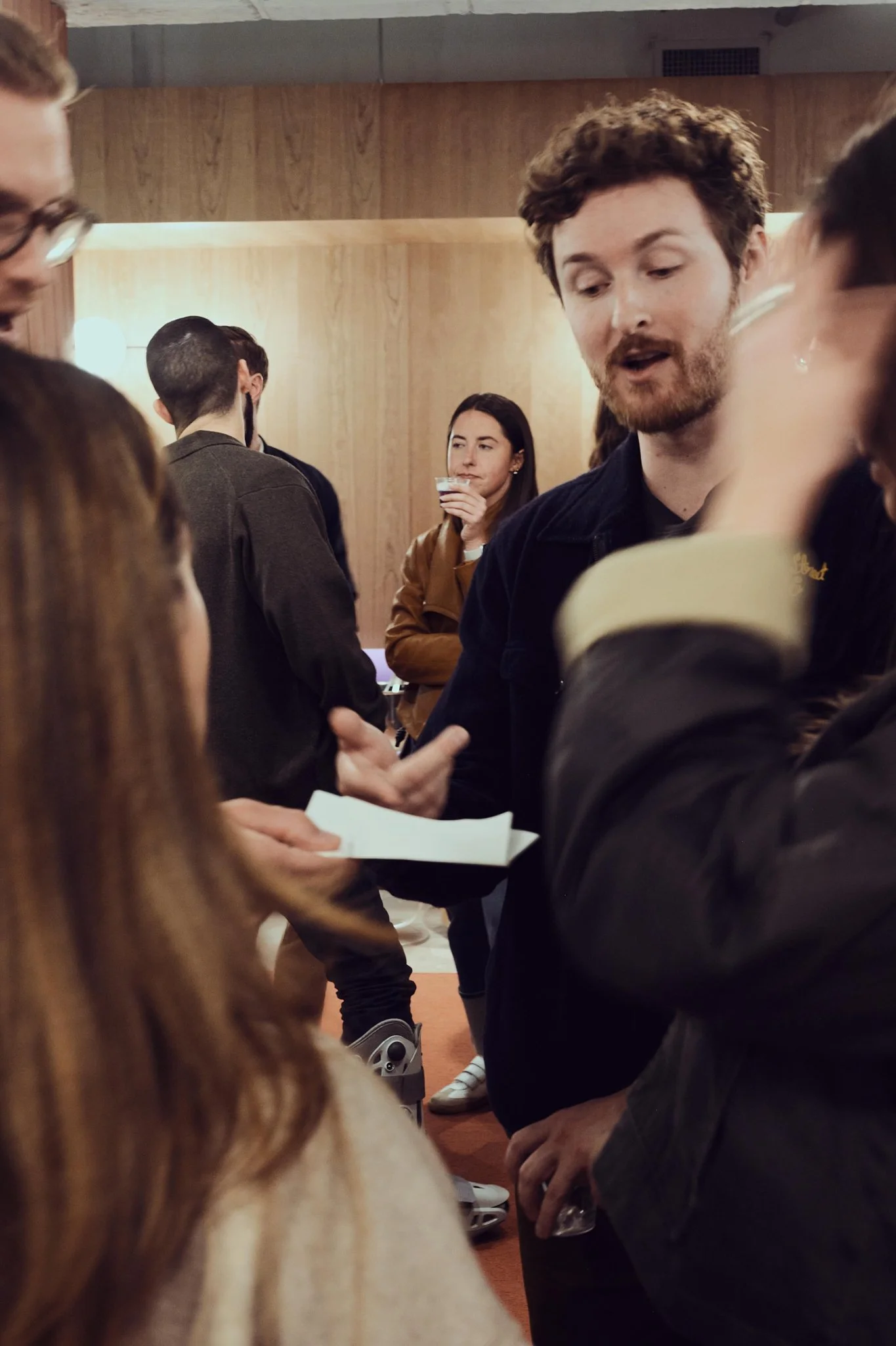 Group of people socializing at an indoor gathering, engaging in conversation with some holding drinks.