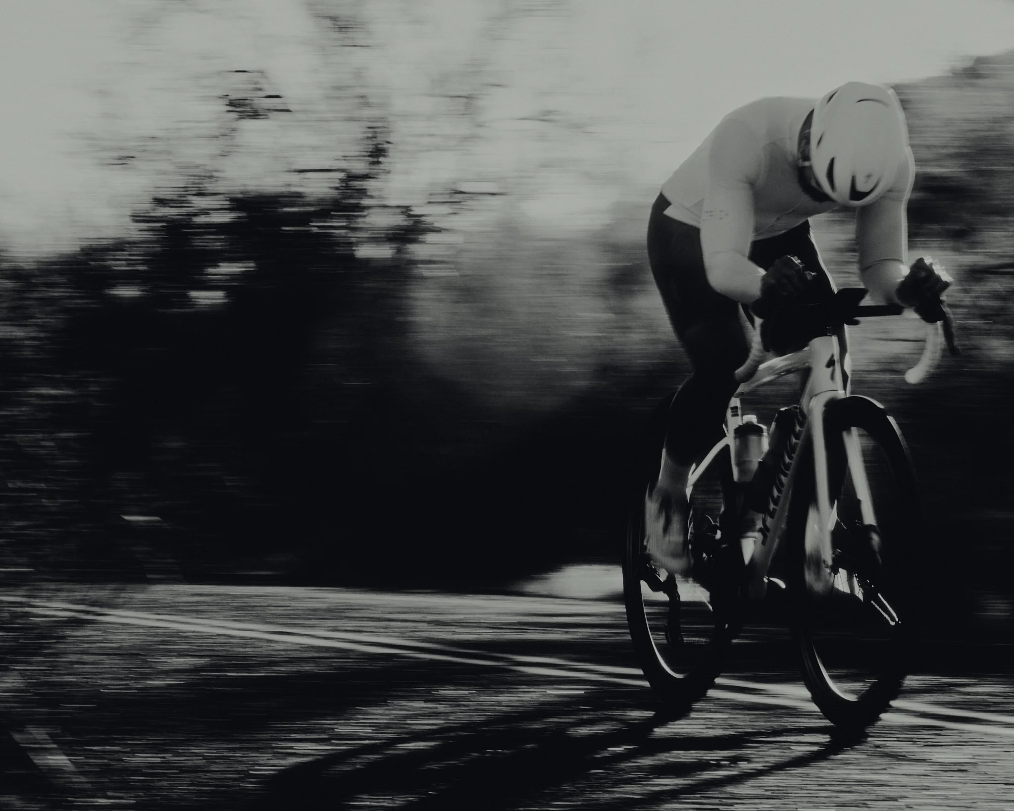 A person wearing a helmet riding a bicycle at high speed, with motion blur suggesting fast movement, in black and white.
