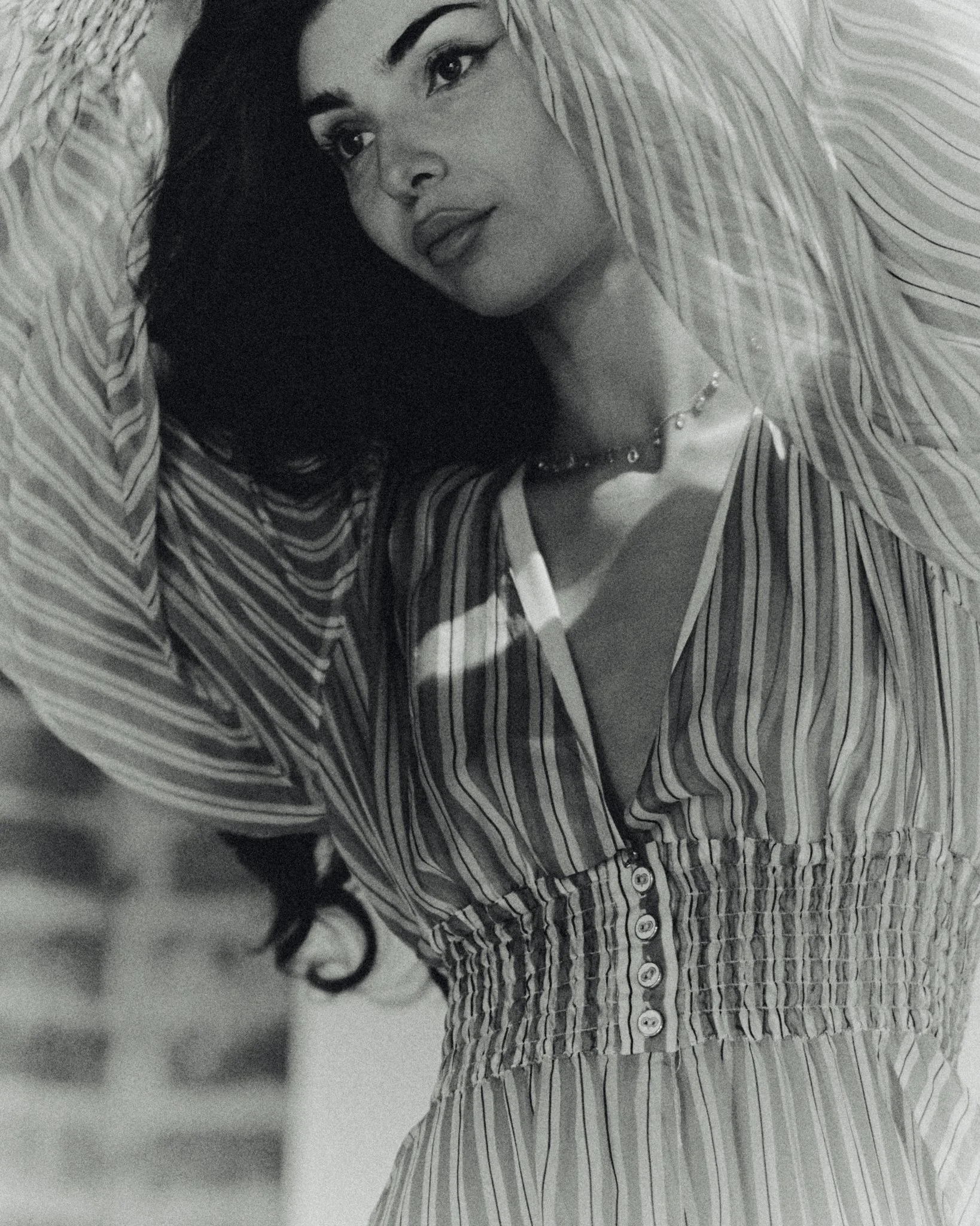 A woman lying on her side on a striped pillow and wearing a striped dress, looking contemplatively away from the camera.