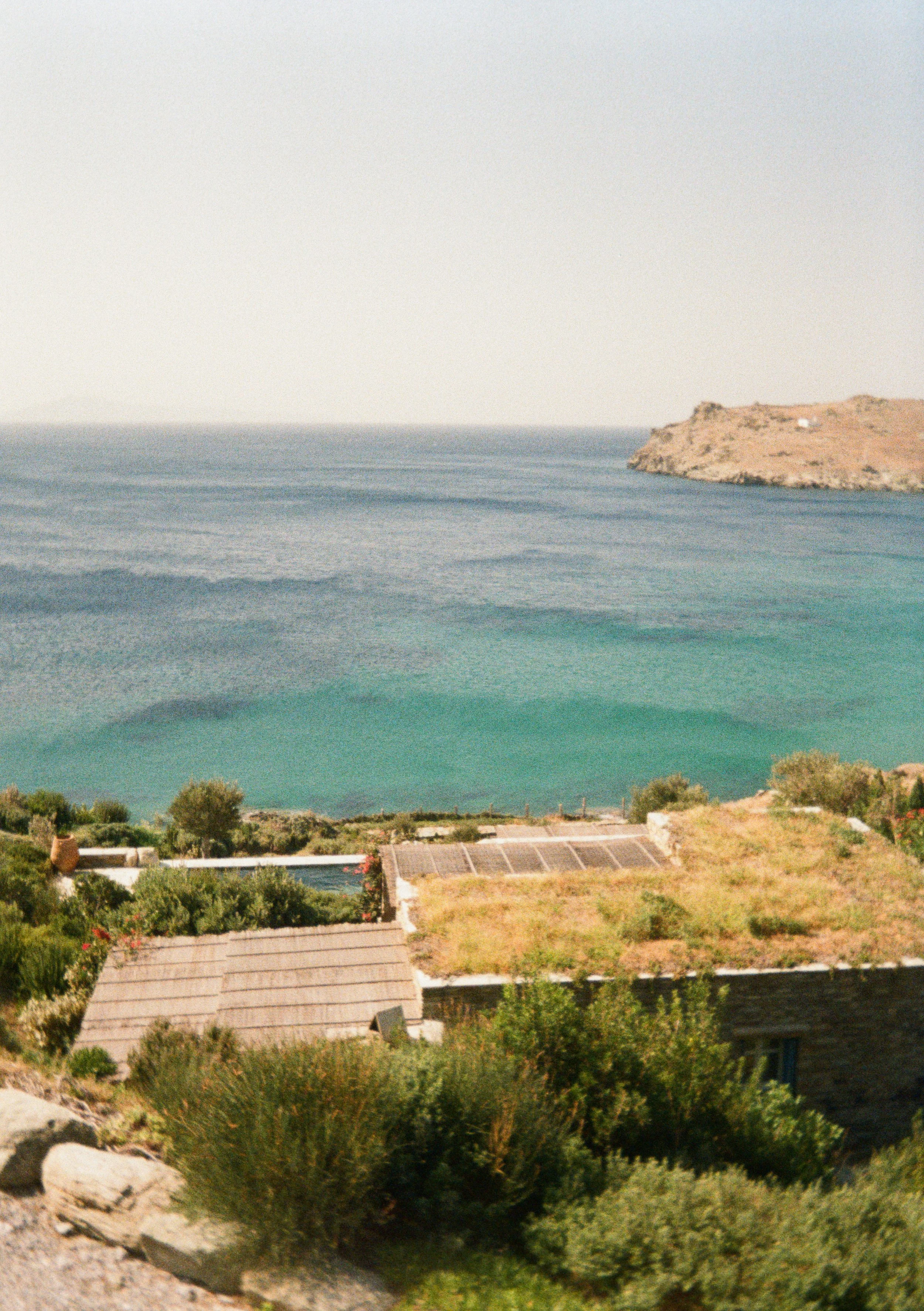 Scenic coastal view with the ocean, a small beach, and greenery surrounding residential buildings.