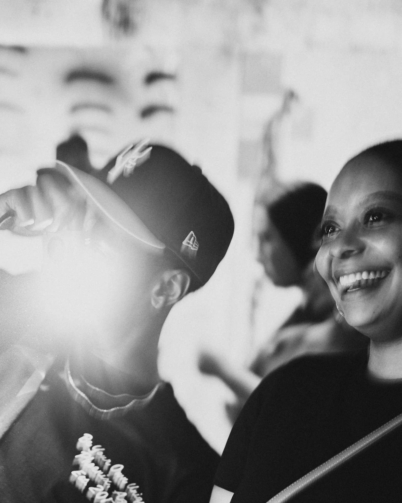 Two women smiling and engaging in conversation, with a blurred person in the background, in a monochrome setting.