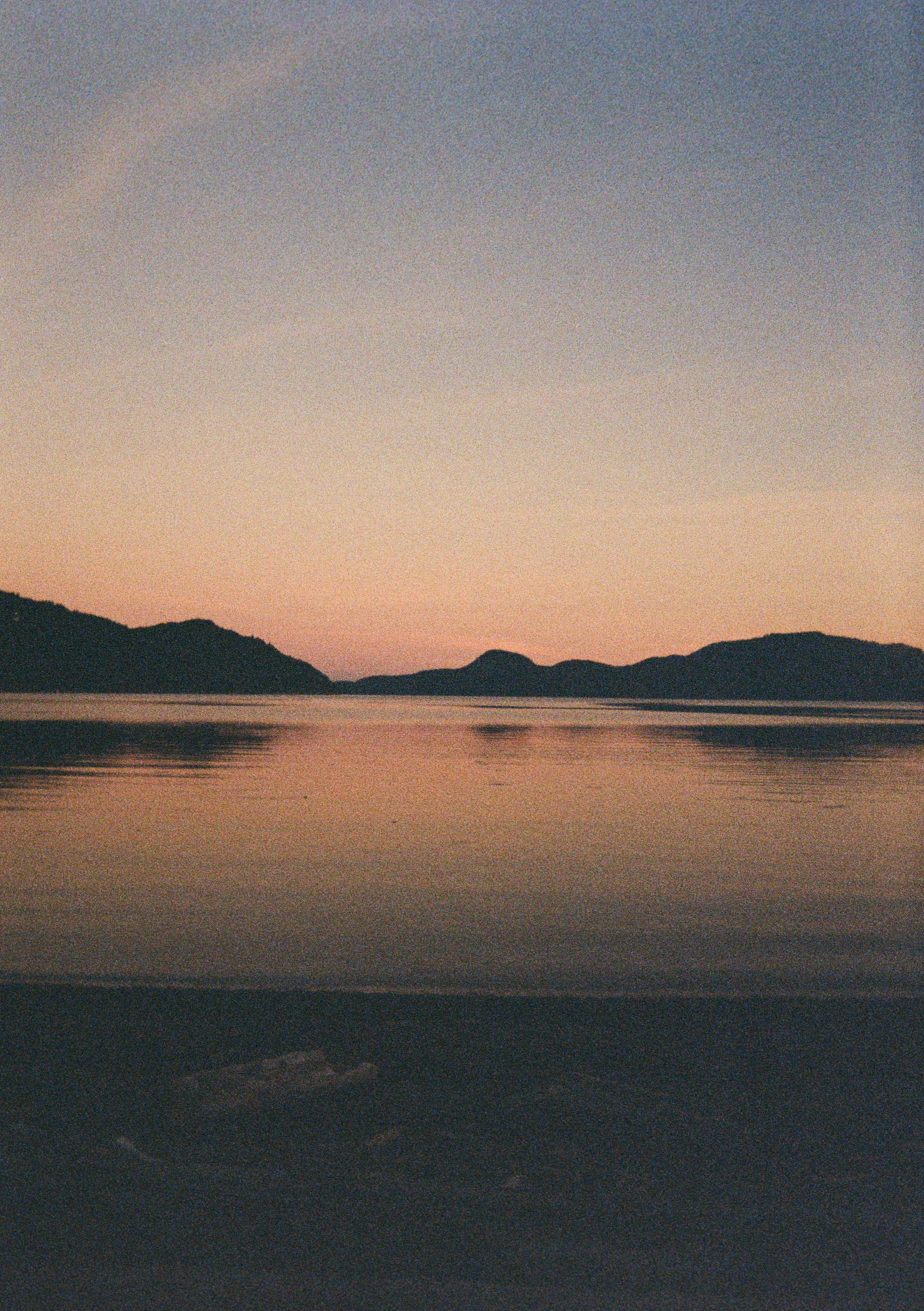 Serene lake scene at sunset with calm water reflecting colorful sky and distant mountains.